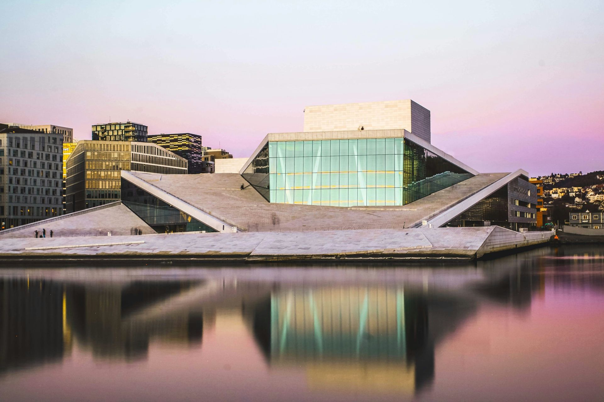 Oslo Opera House, a modern building with a sloping, white exterior, reflected in water at sunset.