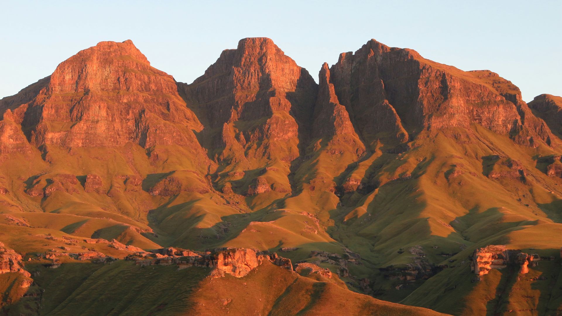Mountains lit by warm sunlight, casting shadows on the green slopes in the Drakensberg, South Africa.