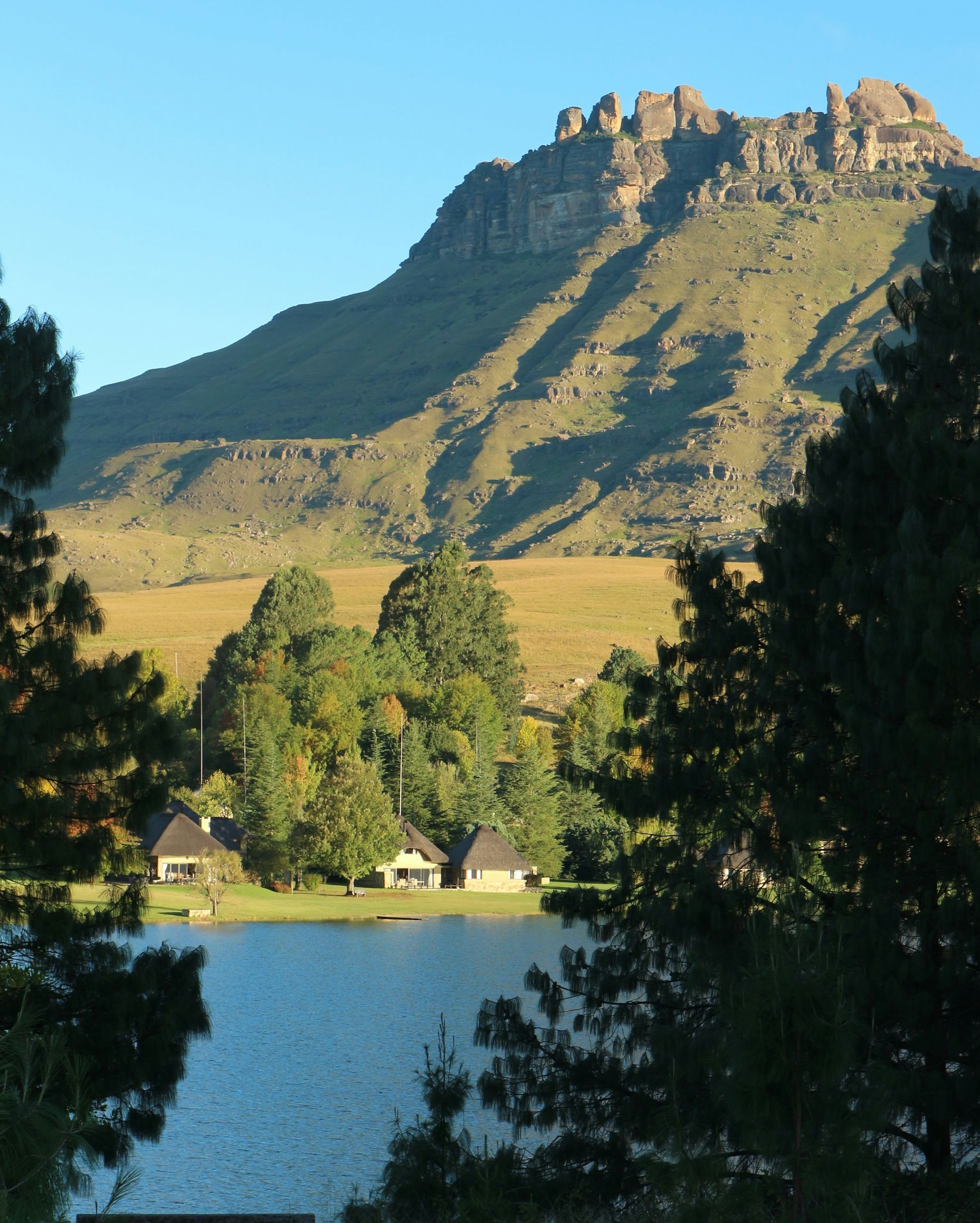 Lake with cabins framed by trees, set against a mountain in the Drakensberg, South Africa.