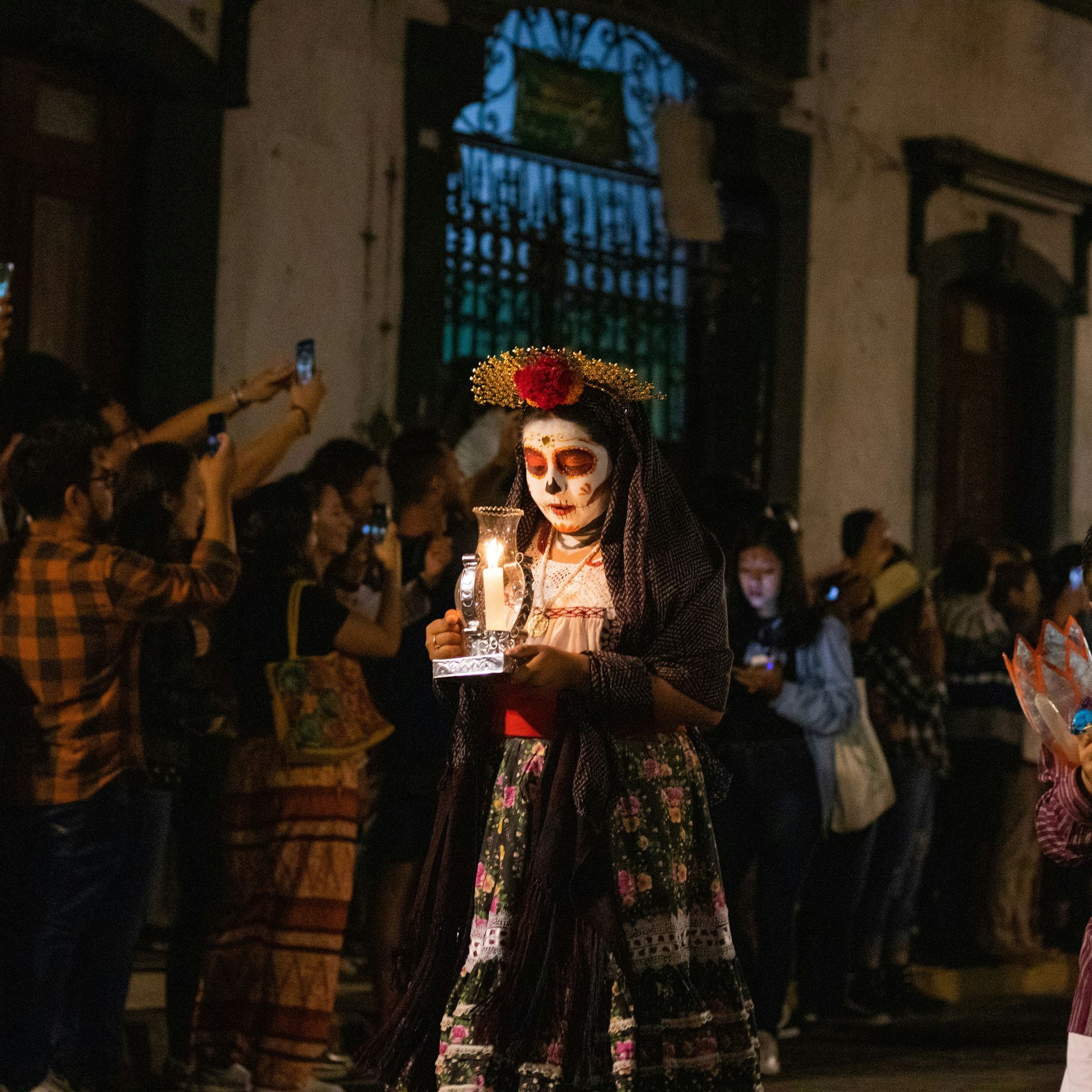 Woman in Catrina makeup holding a candle, leading a procession at night in Oaxaca, Mexico.