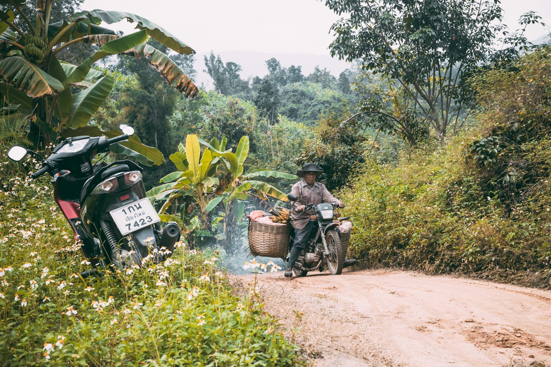 A man is riding a motorcycle down a dirt road in Pai, Thailand.