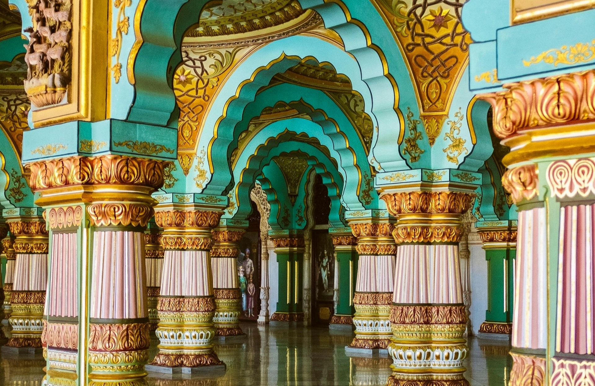 Ornate teal and gold arches and columns inside a palace, with a glossy floor reflecting the scene in India.