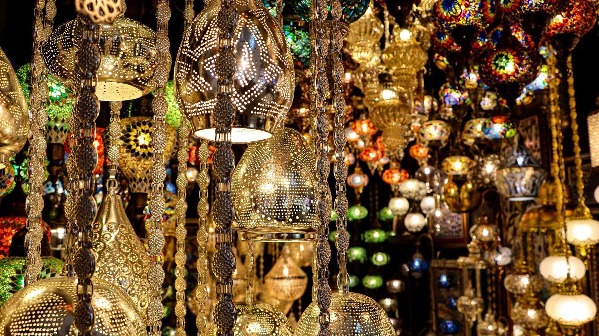 Ornate, colorful hanging lamps with intricate designs, illuminated in a shop in Turkey.
