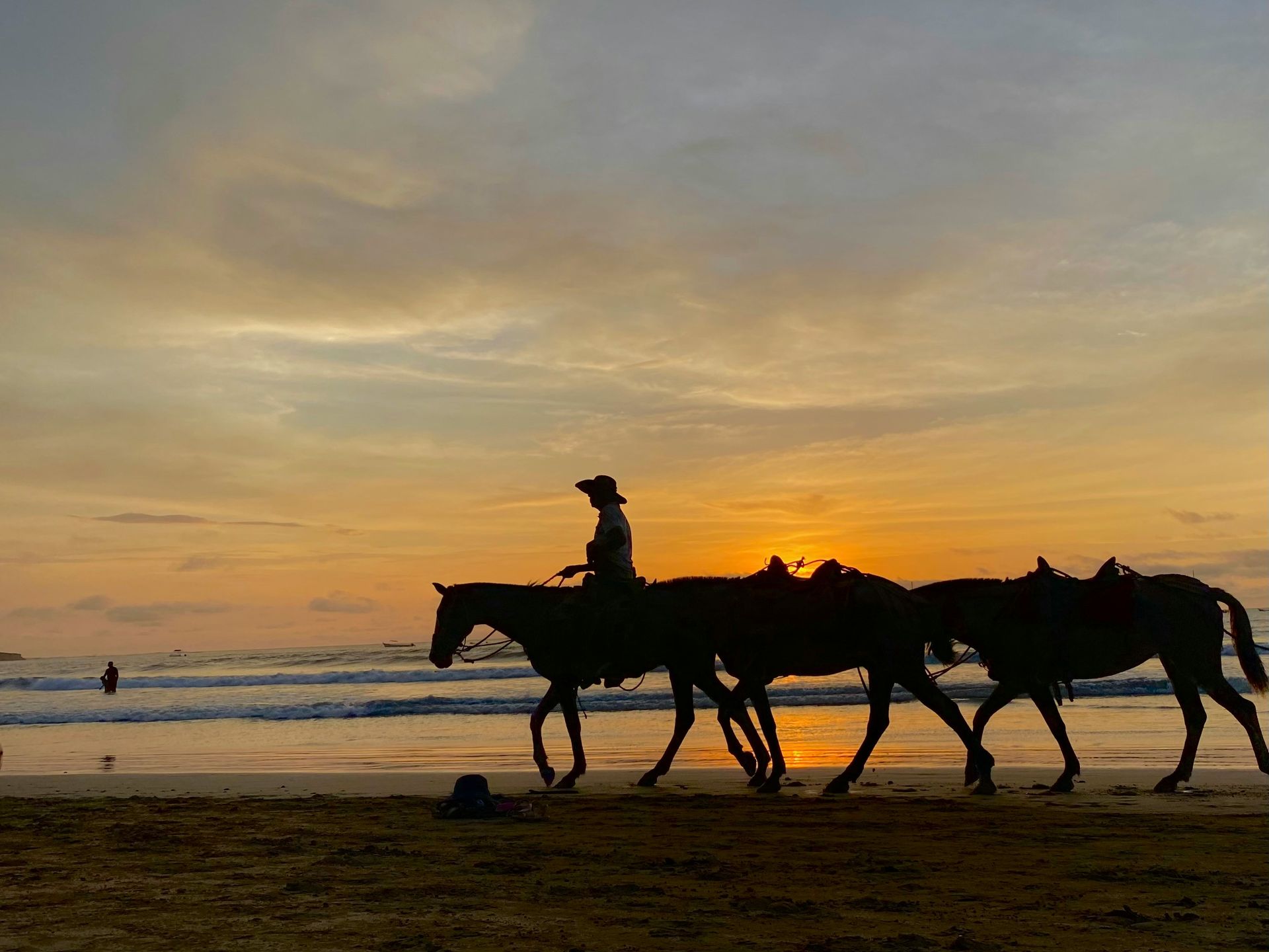 Silhouetted rider on horseback leading two horses along a beach at sunset in Tamarindo, Costa Rica.