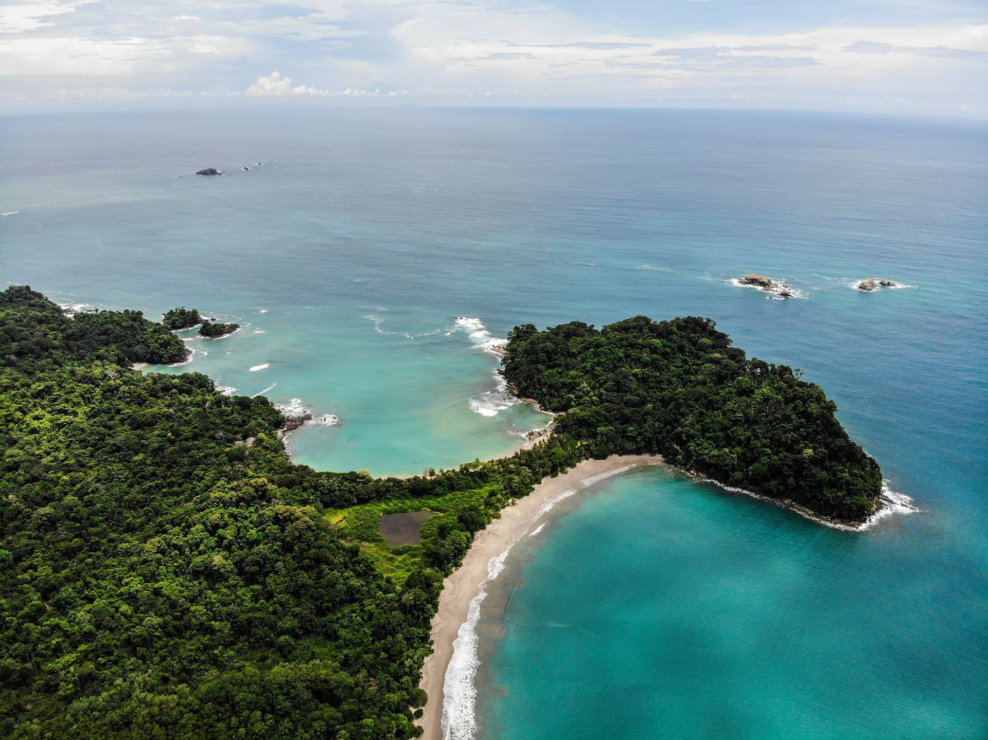 Aerial view of a tropical coastline with a beach and turquoise water. Dense green jungle covers the land in Manuel Antonio, Costa Rica.