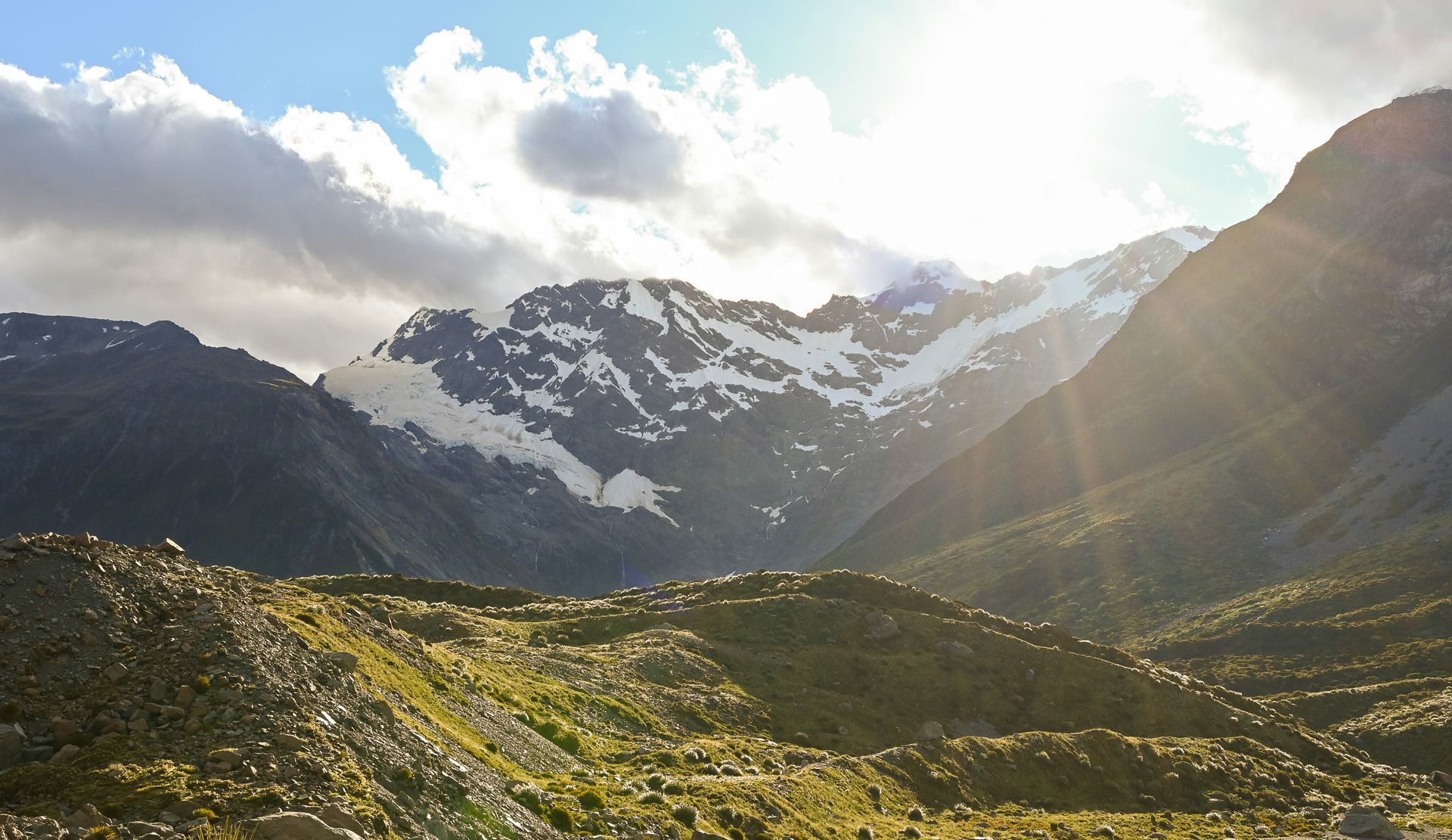 The sun is shining through the clouds over the mountains in Mount Cook National Park, New Zealand.
