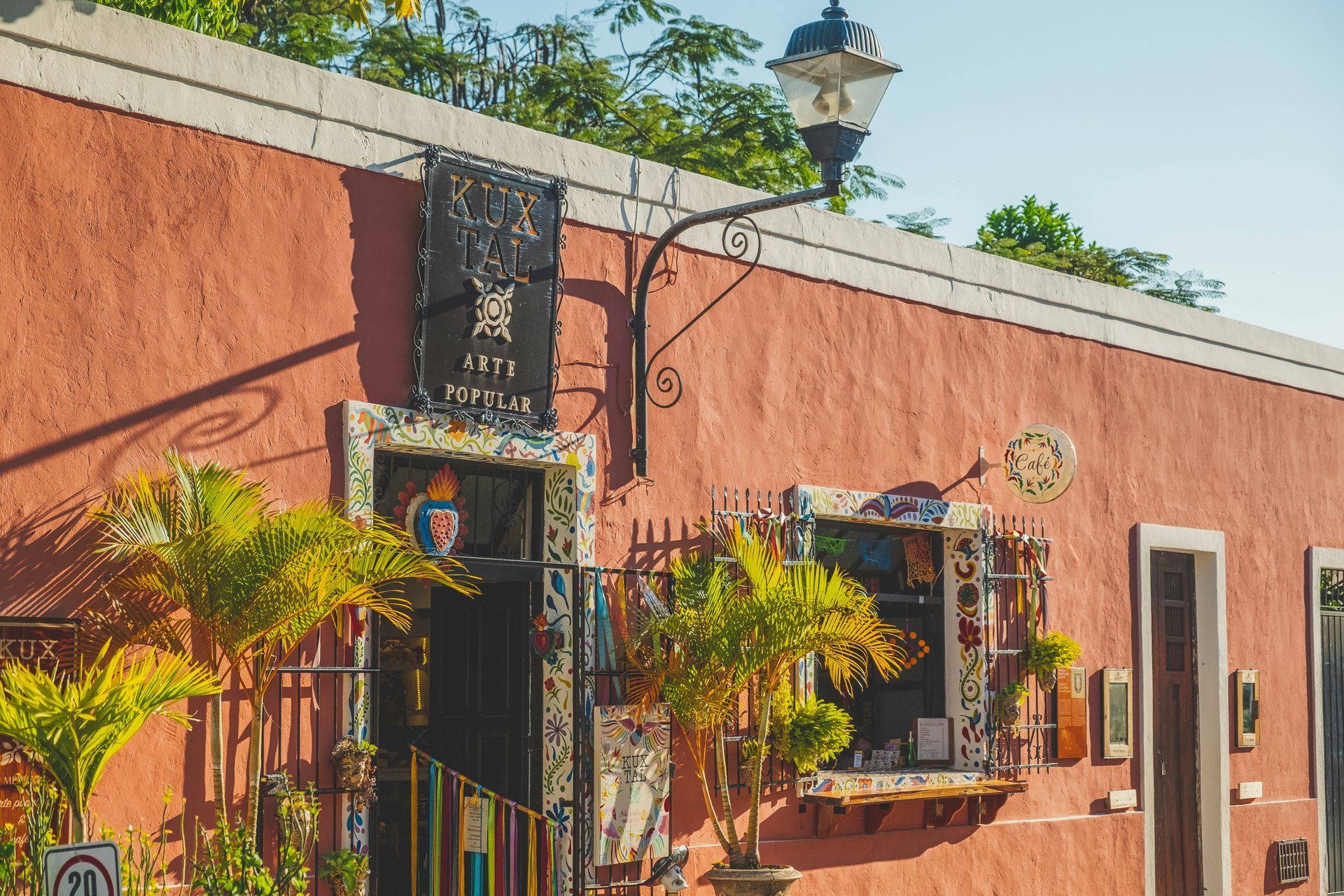 Exterior of a salmon-colored building with tile-framed windows and door, with palm trees in front in Valladolid, Mexico.