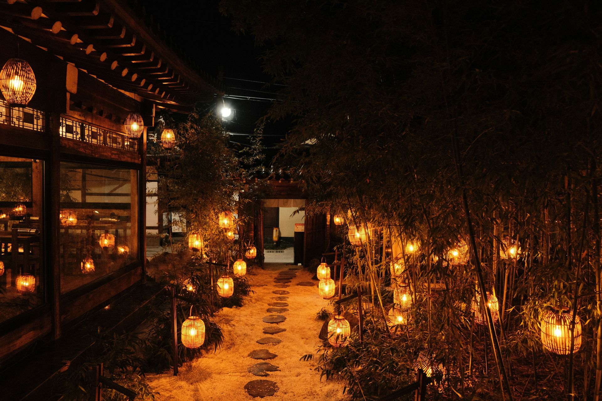 Stone path illuminated by lanterns at night, leading to an open doorway between bamboo in Gyeongju, South Korea.