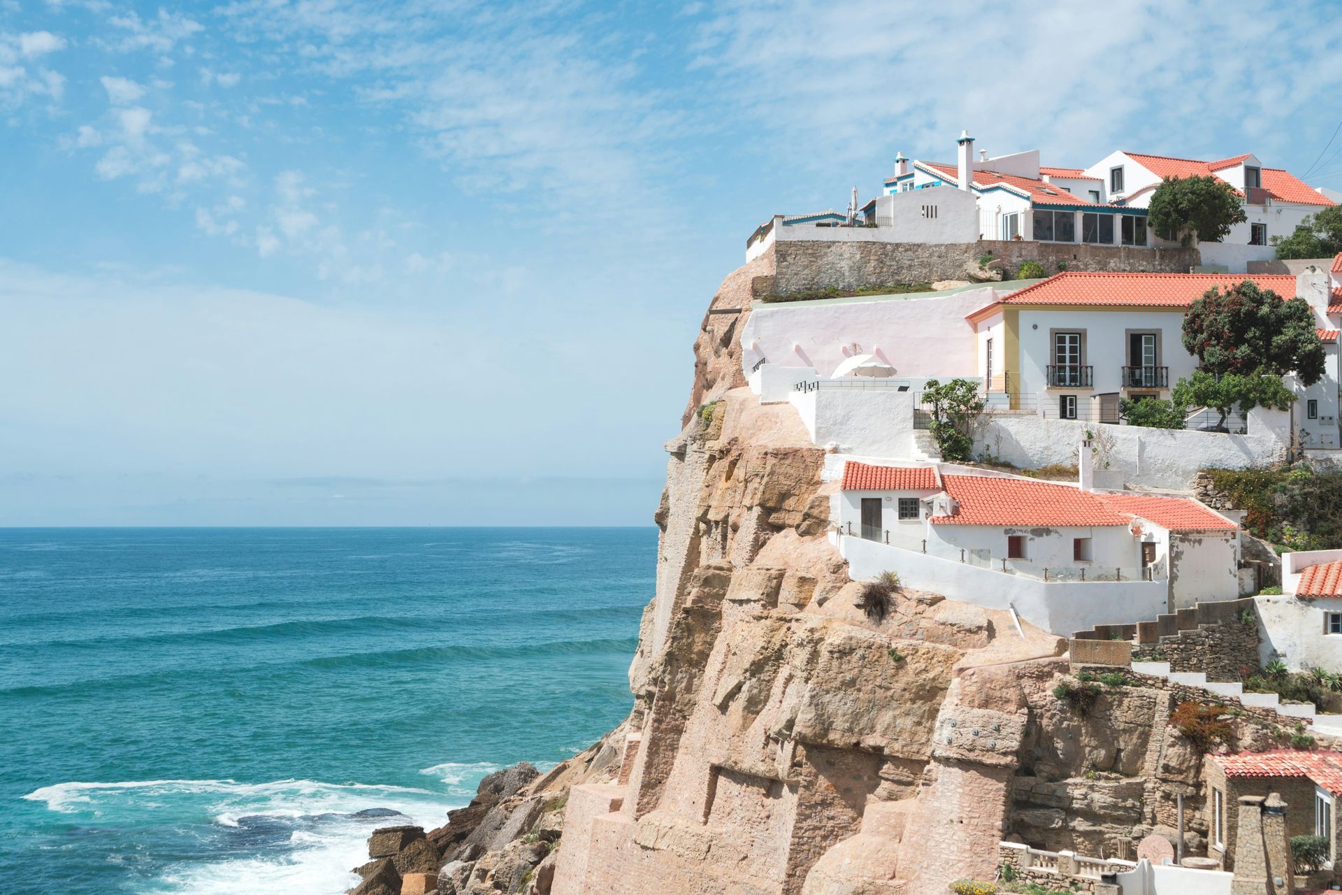 White houses with orange roofs perched on a cliff overlooking the ocean in Azenhas do Mar, Portugal.