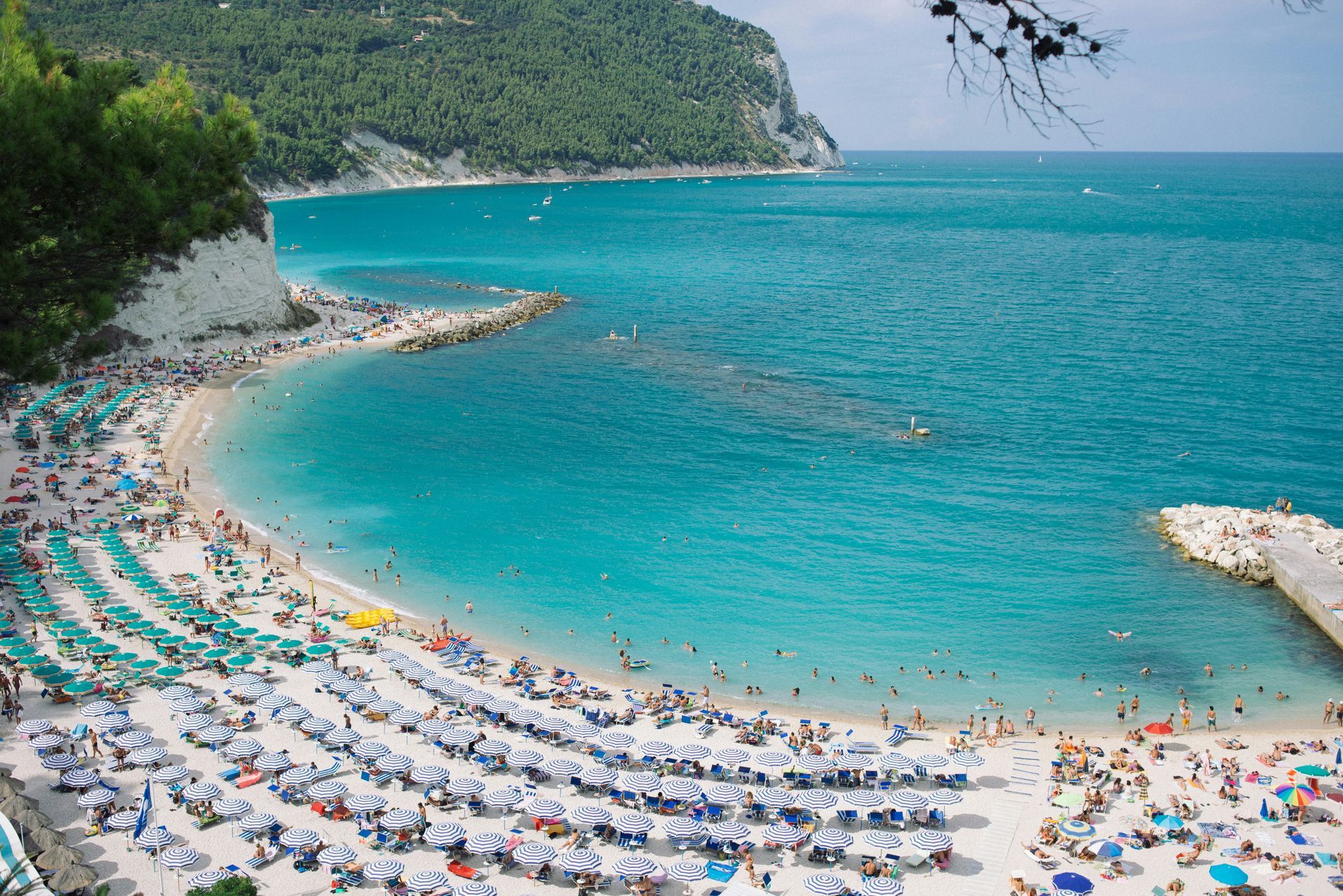 A beach filled with lots of people and umbrellas in Sirolo, Italy