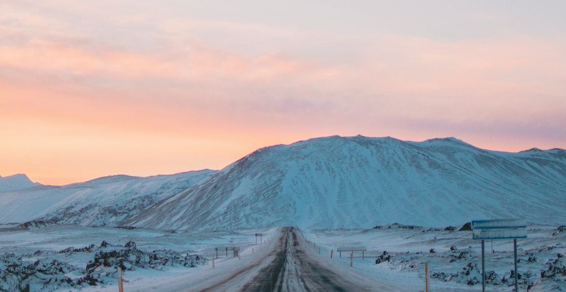 Snow-covered mountains and road under a pastel sky at sunrise in Iceland.