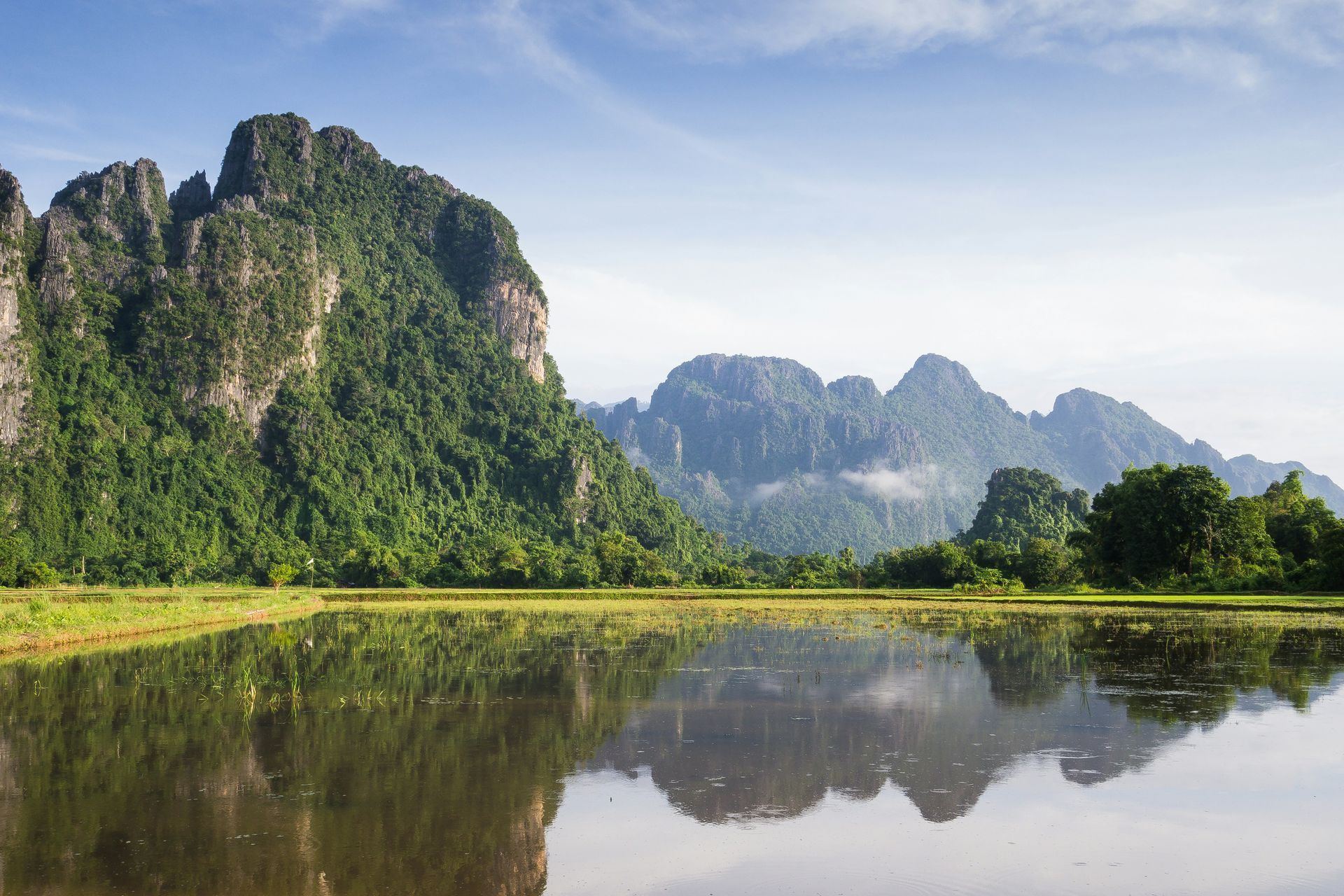 Mountains reflected in water, with lush green vegetation in Vang Vieng, Laos.