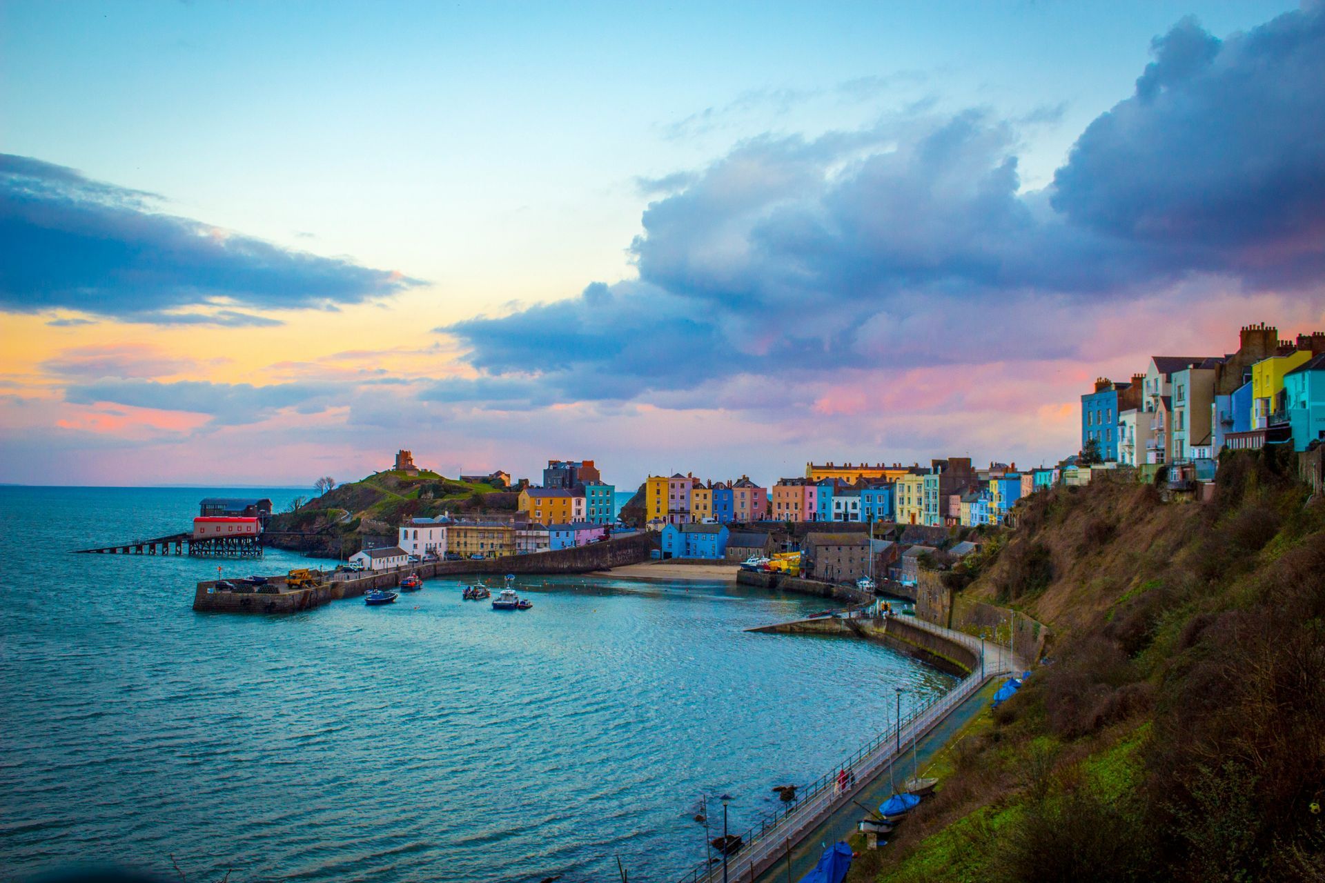 Coastal town of Tenby, Wales, colorful buildings overlooking a bay under a cloudy, sunset sky.