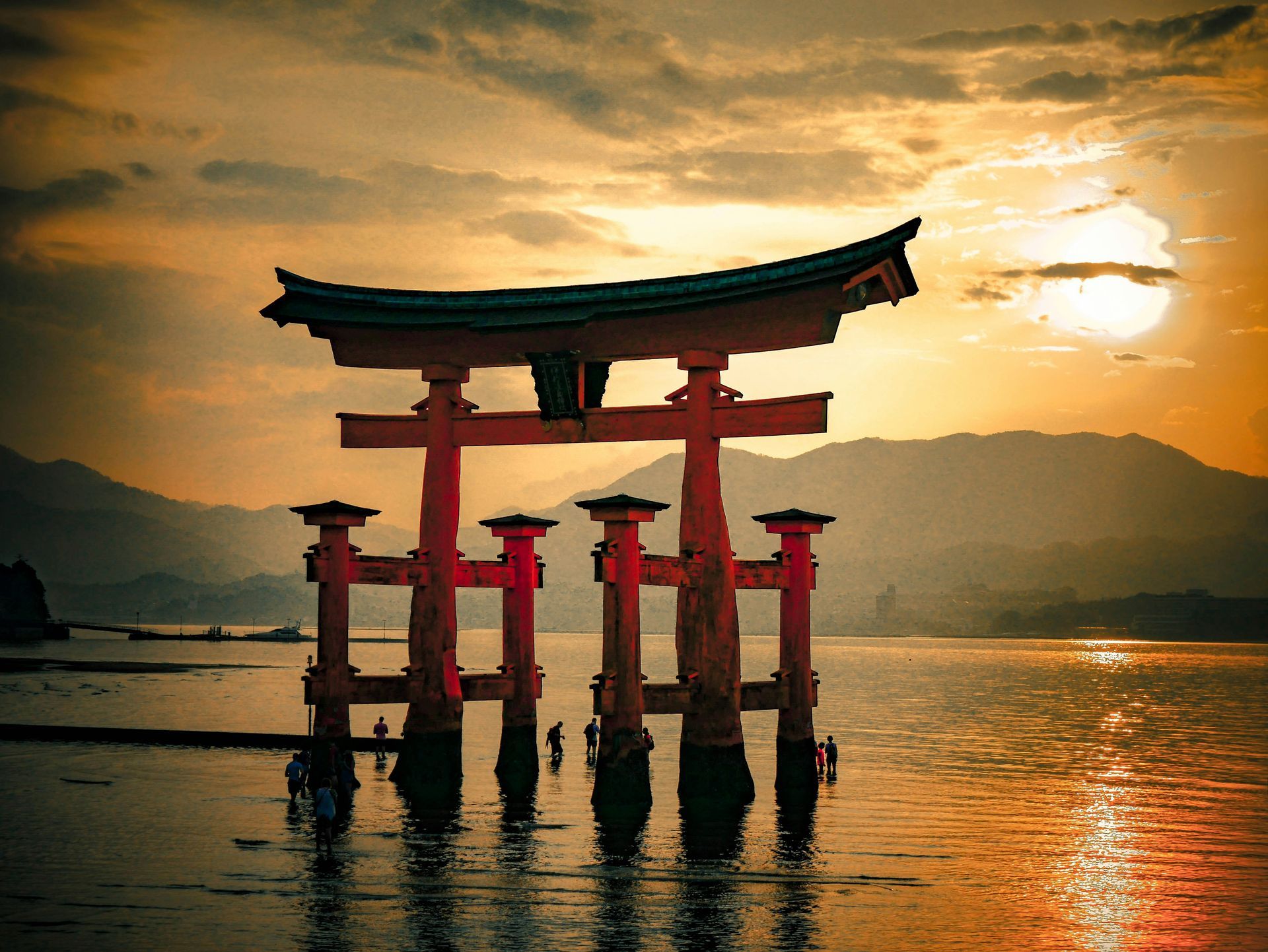 Red torii gate in water at sunset, with mountains in the background in Hiroshima, Japan.
