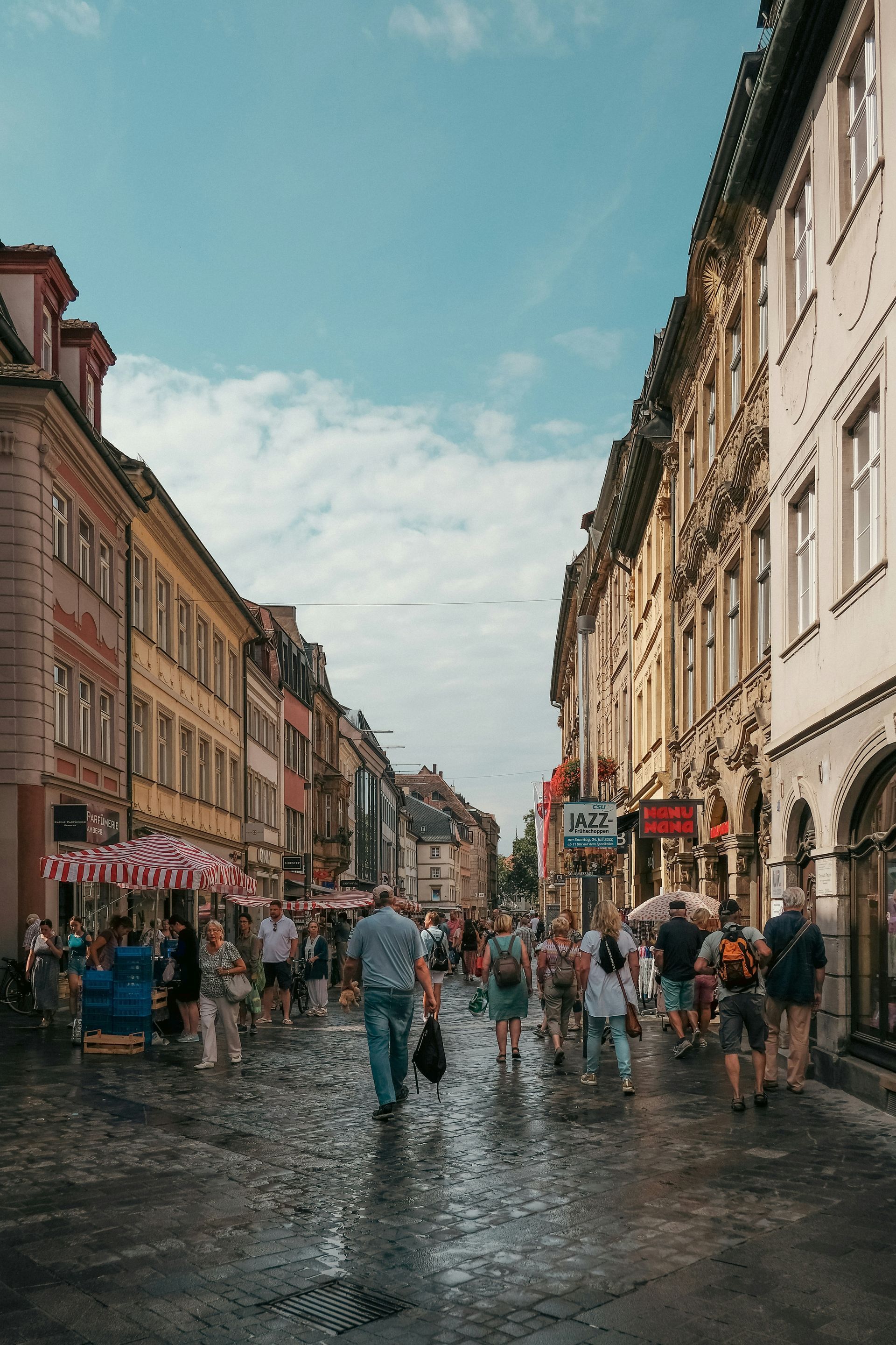 People walking on a cobblestone street in Trier, Germany with shops and colorful buildings.