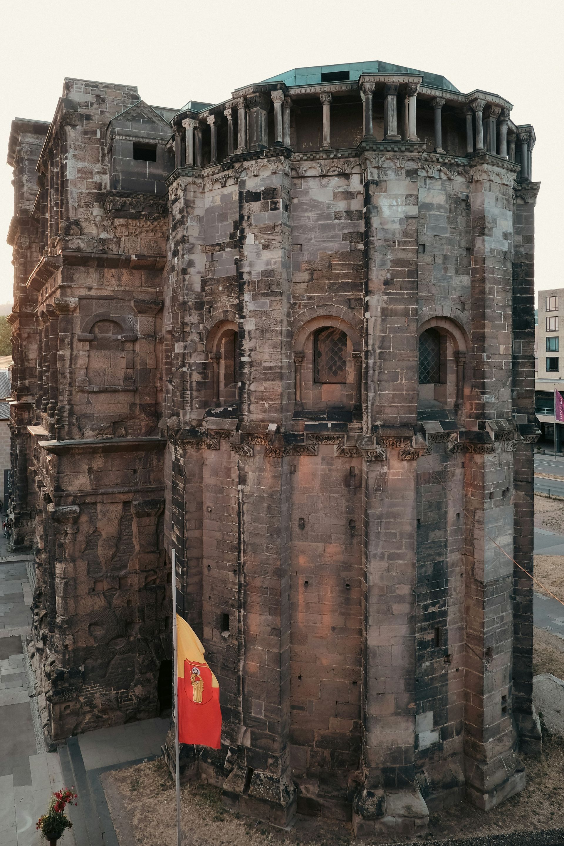 Ruined stone building with flag, possibly in Trier, Germany. Tall and cylindrical with arched windows.
