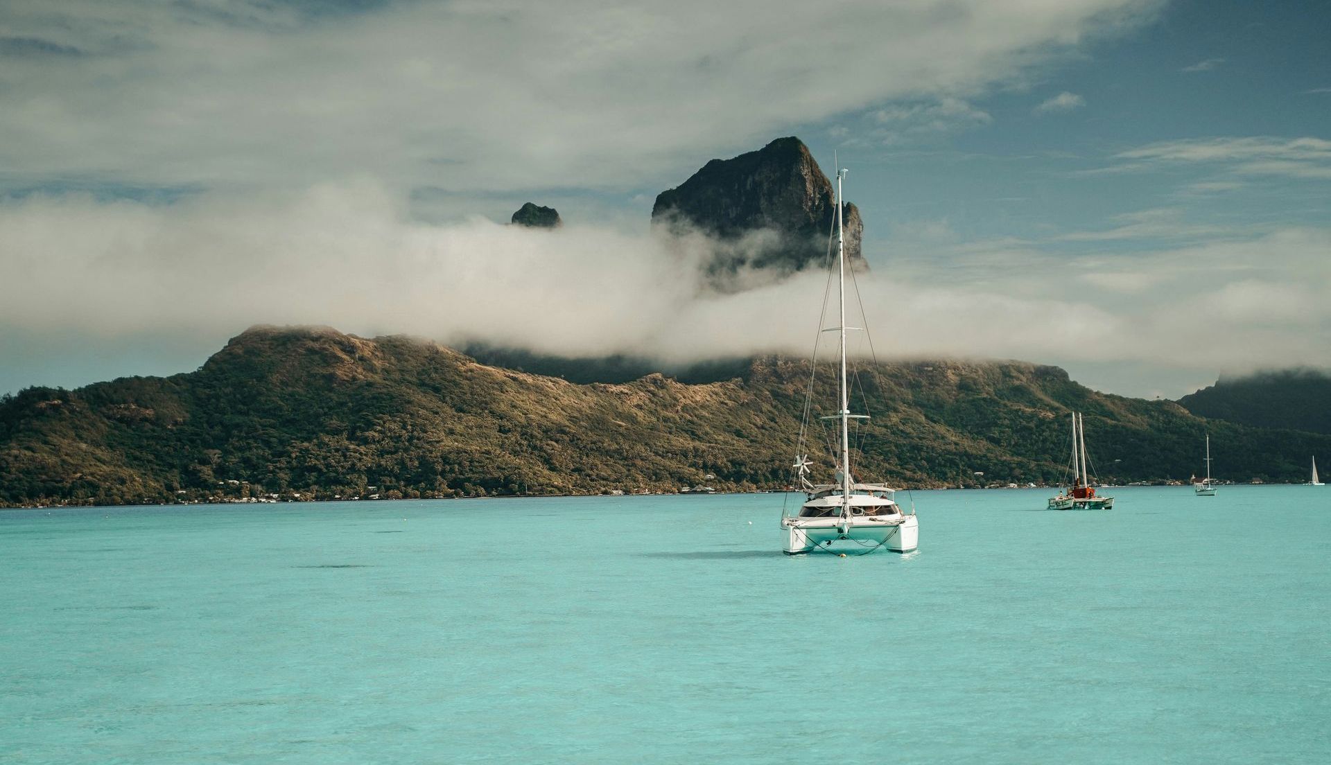 A sailboat is floating in the ocean with a mountain in the background in French Polynesia. 