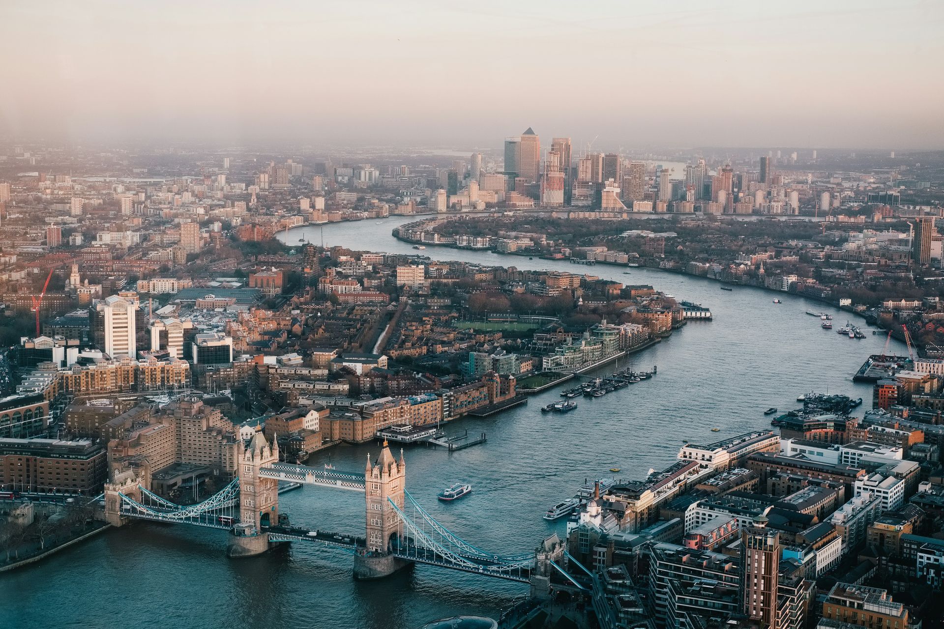 London cityscape, Thames River flowing past Tower Bridge, with buildings under a hazy sky.