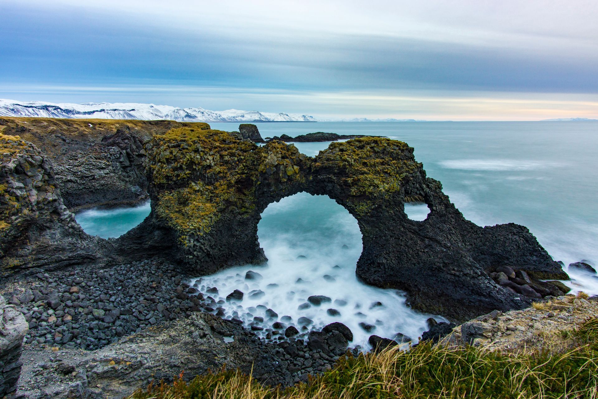 Sea arch in Iceland with waves crashing through, under a cloudy sky in Snæfellsnes, Iceland.