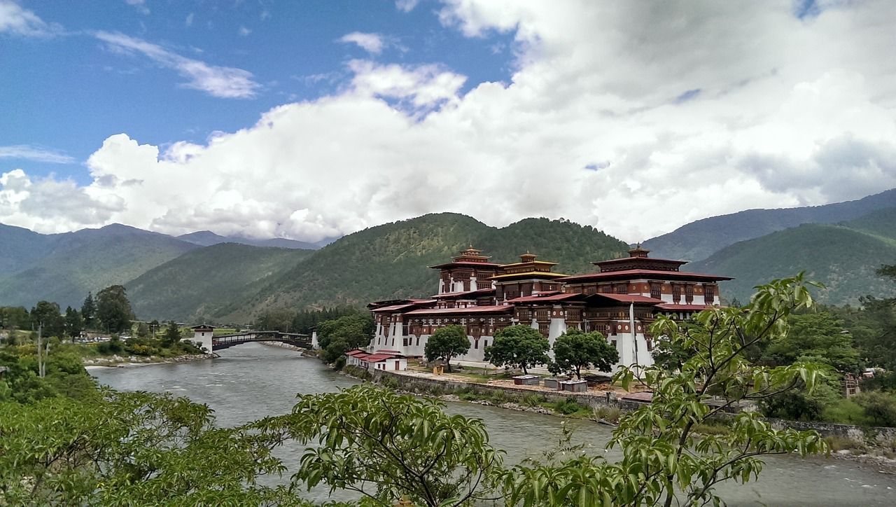 A large building is sitting on the shore of a river with mountains in the background in Bhutan.