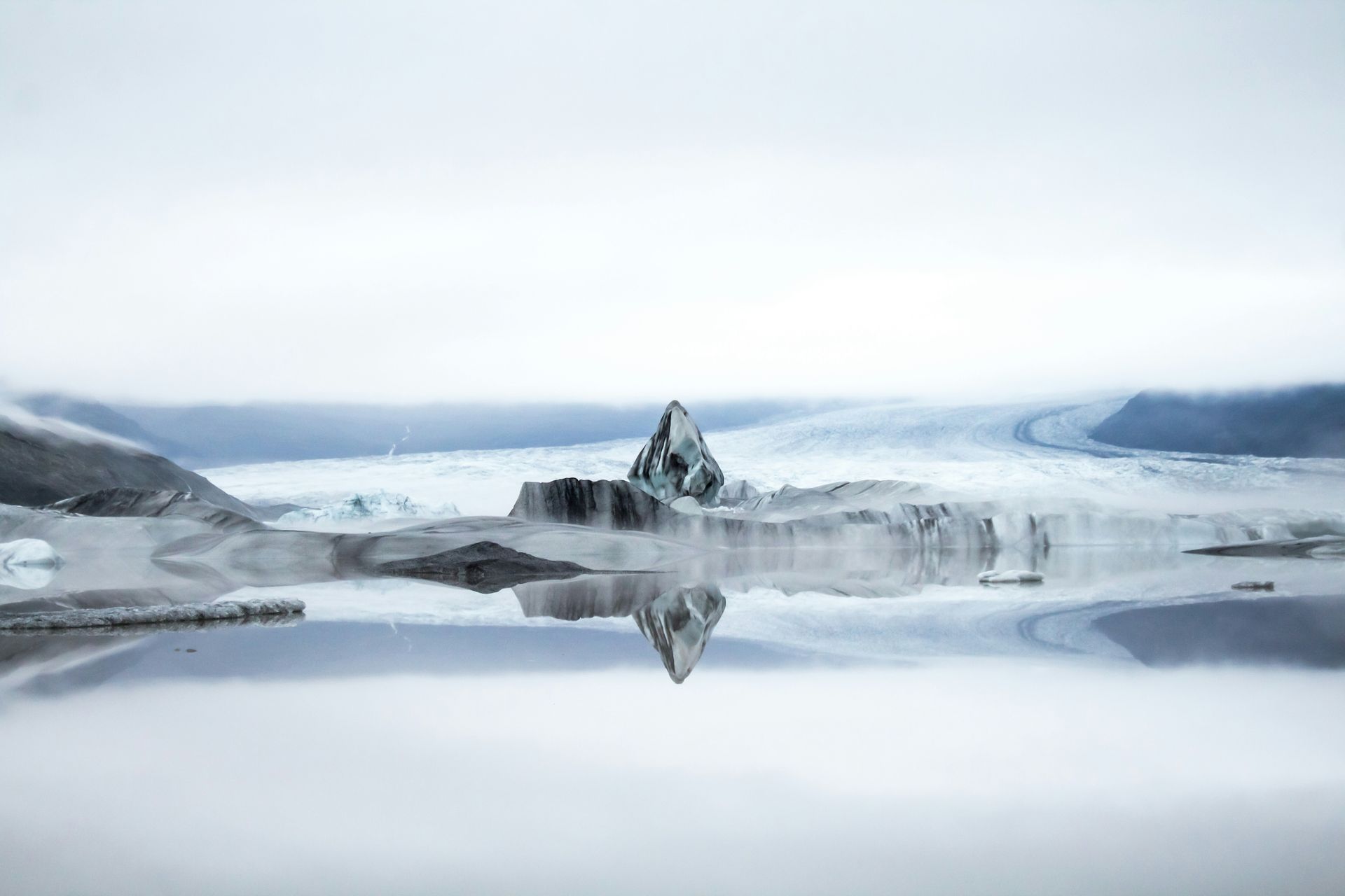 Glacial landscape: Icebergs on a reflective lake, shrouded in mist, surrounded by snow-covered mountains at Vatnajökull National Park, Iceland.