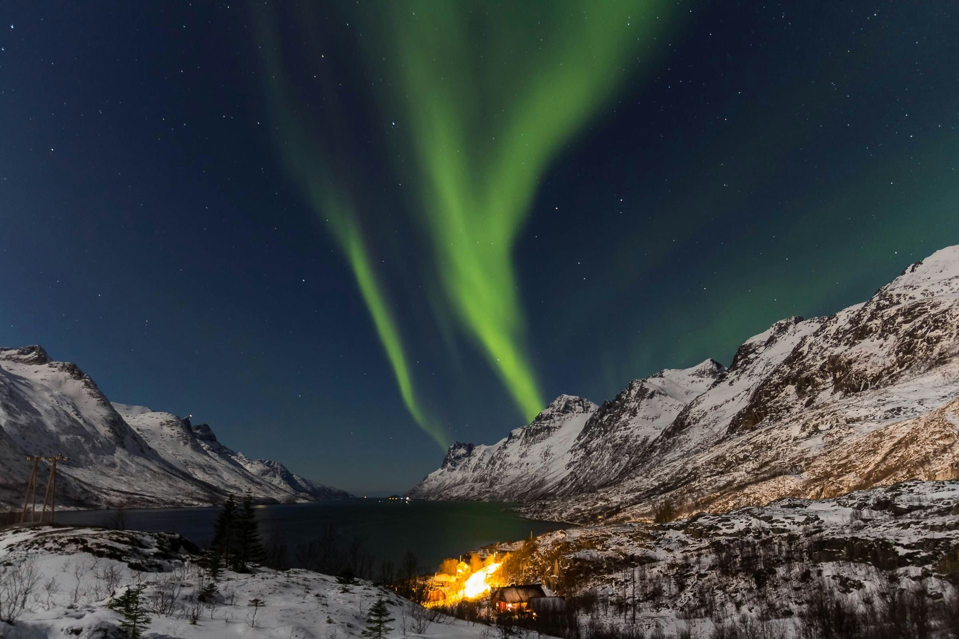 Northern lights dance above snowy mountains and a lake in Tromsø, Norway.