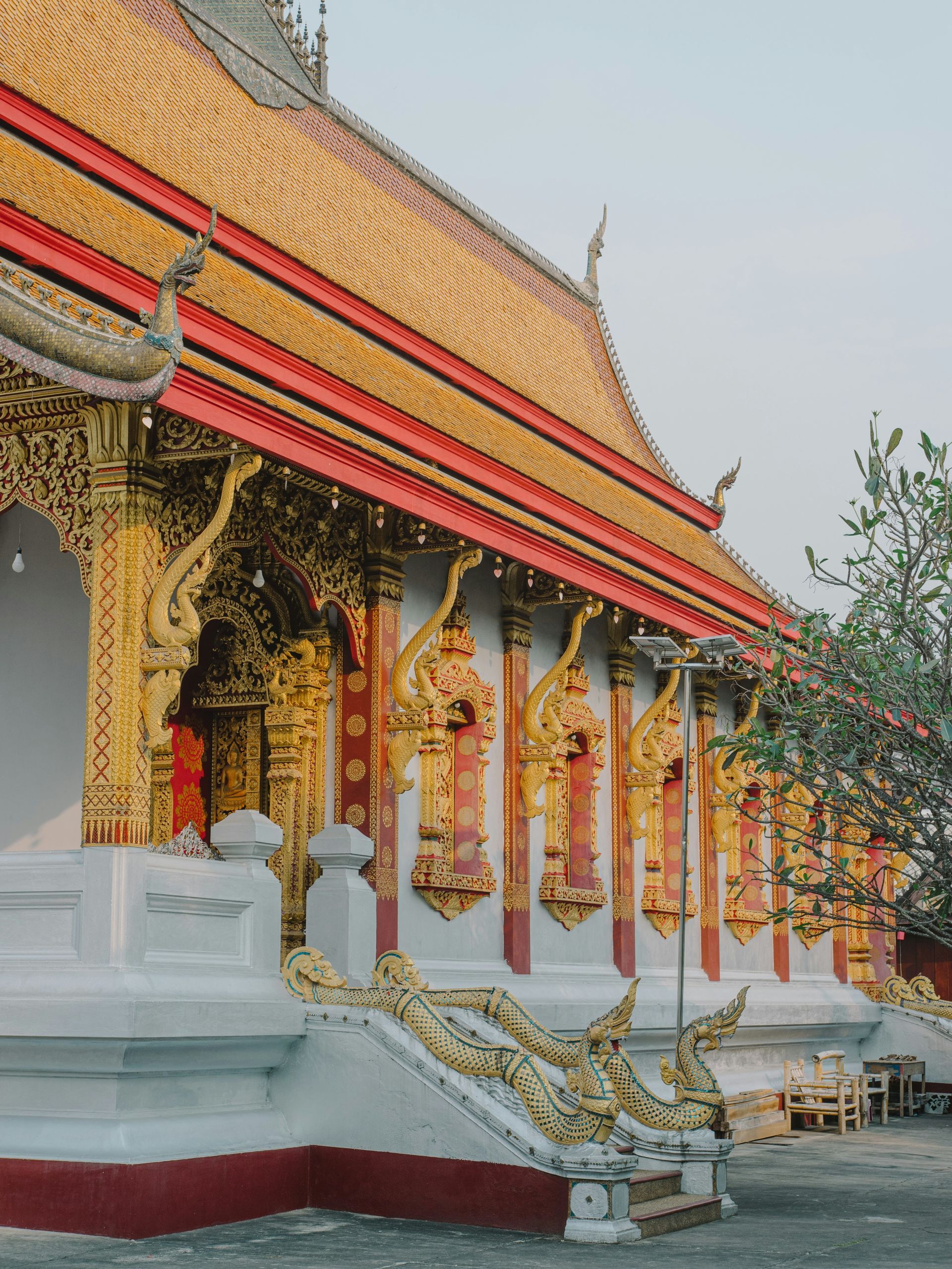 Ornate golden and red temple in Thailand, with a sloping roof and white pillars in Luang Prabang, Laos.