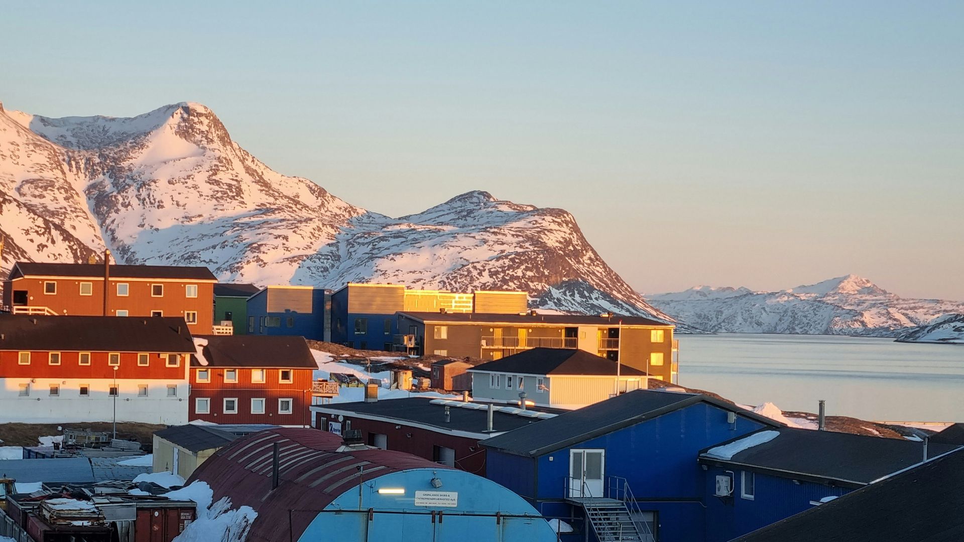 Colorful buildings nestled below snow-covered mountains near the sea in Nuuk, Greenland.