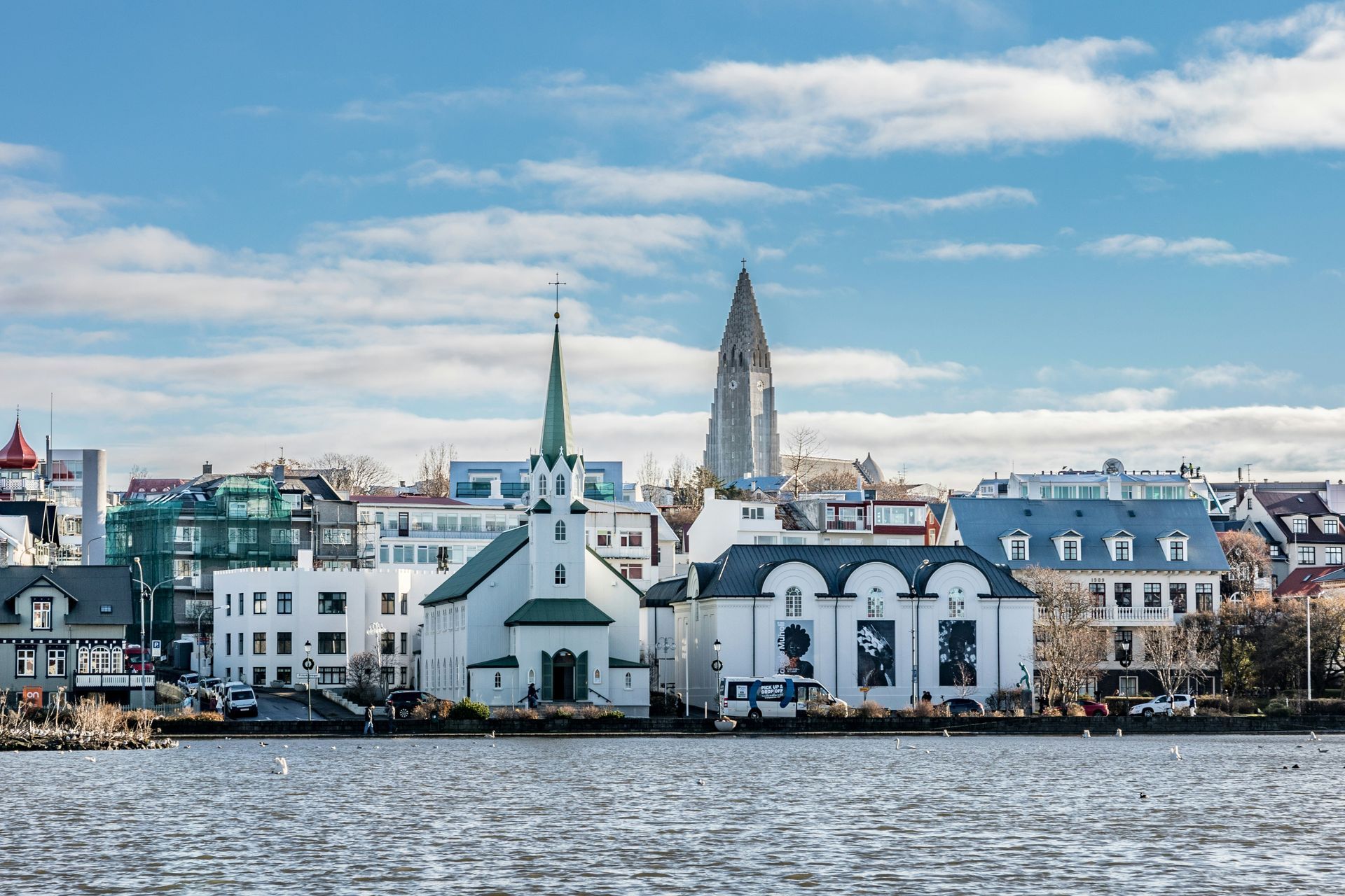 City skyline of Reykjavik, Iceland, with church steeples, colorful buildings, and blue sky reflecting in the water.