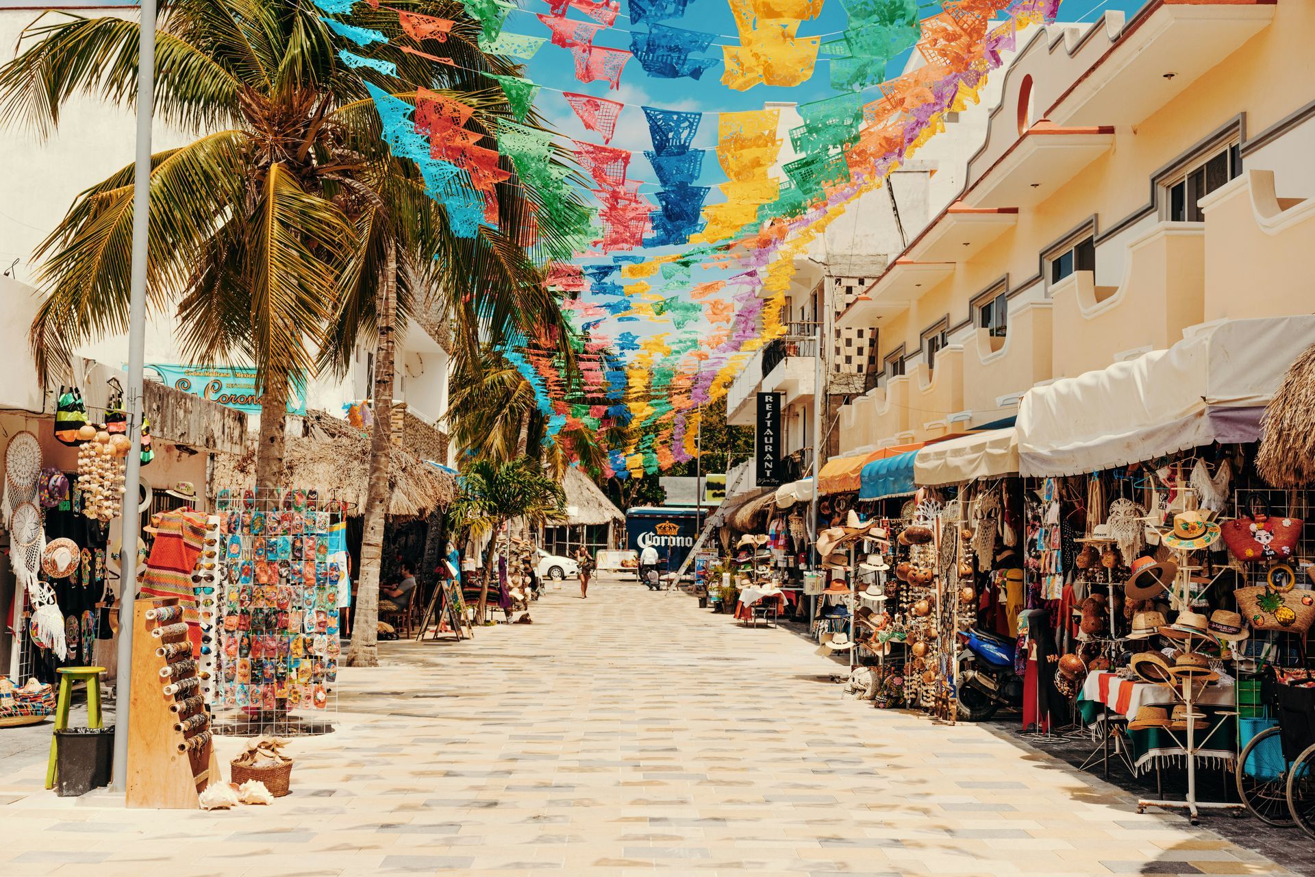 A colorful street market lined with shops under strings of decorative flags in Playa del Carmen, Mexico.