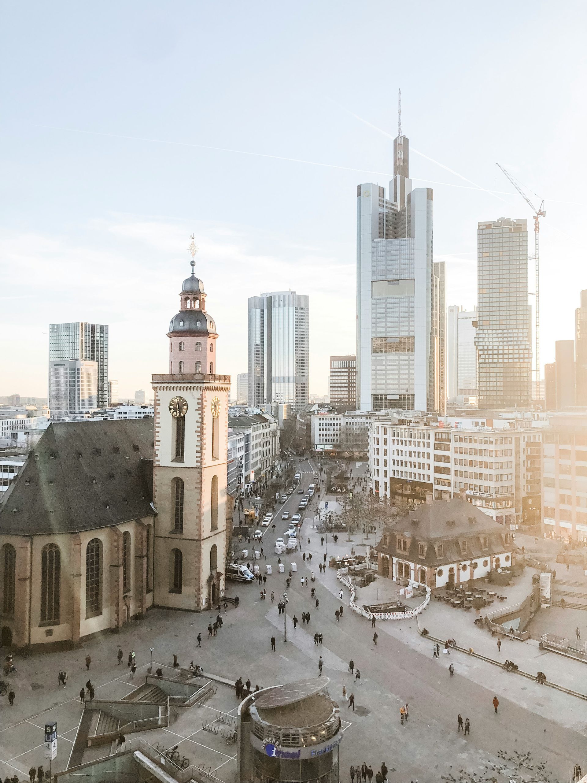 Frankfurt skyline with church and modern skyscrapers, bustling city square. Sunny day.