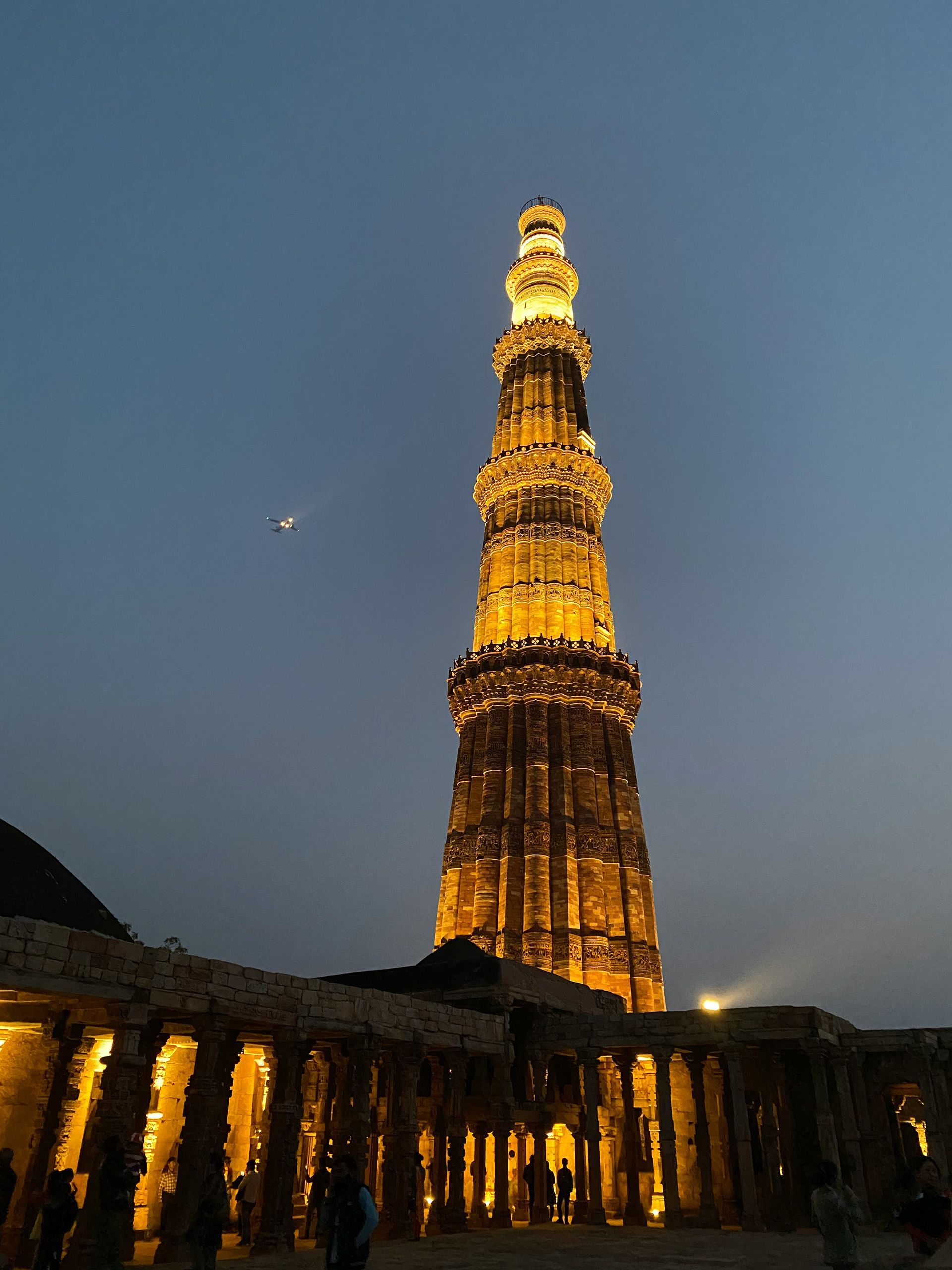 Qutub Minar, Delhi, lit up at dusk. Tall minaret against a dark blue sky.