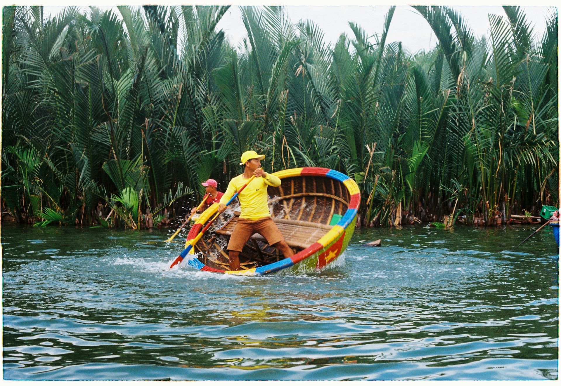 Two people in a colorful round boat on water, surrounded by lush greenery in Hội An, Vietnam.