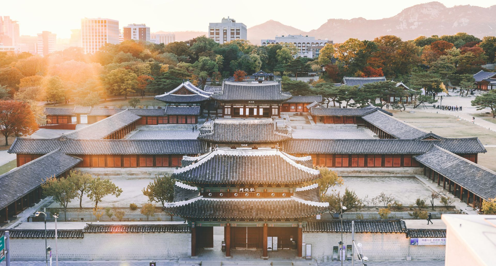 Traditional Korean palace complex bathed in warm sunlight; buildings with tiled roofs and wooden structures in Seoul, South Korea.