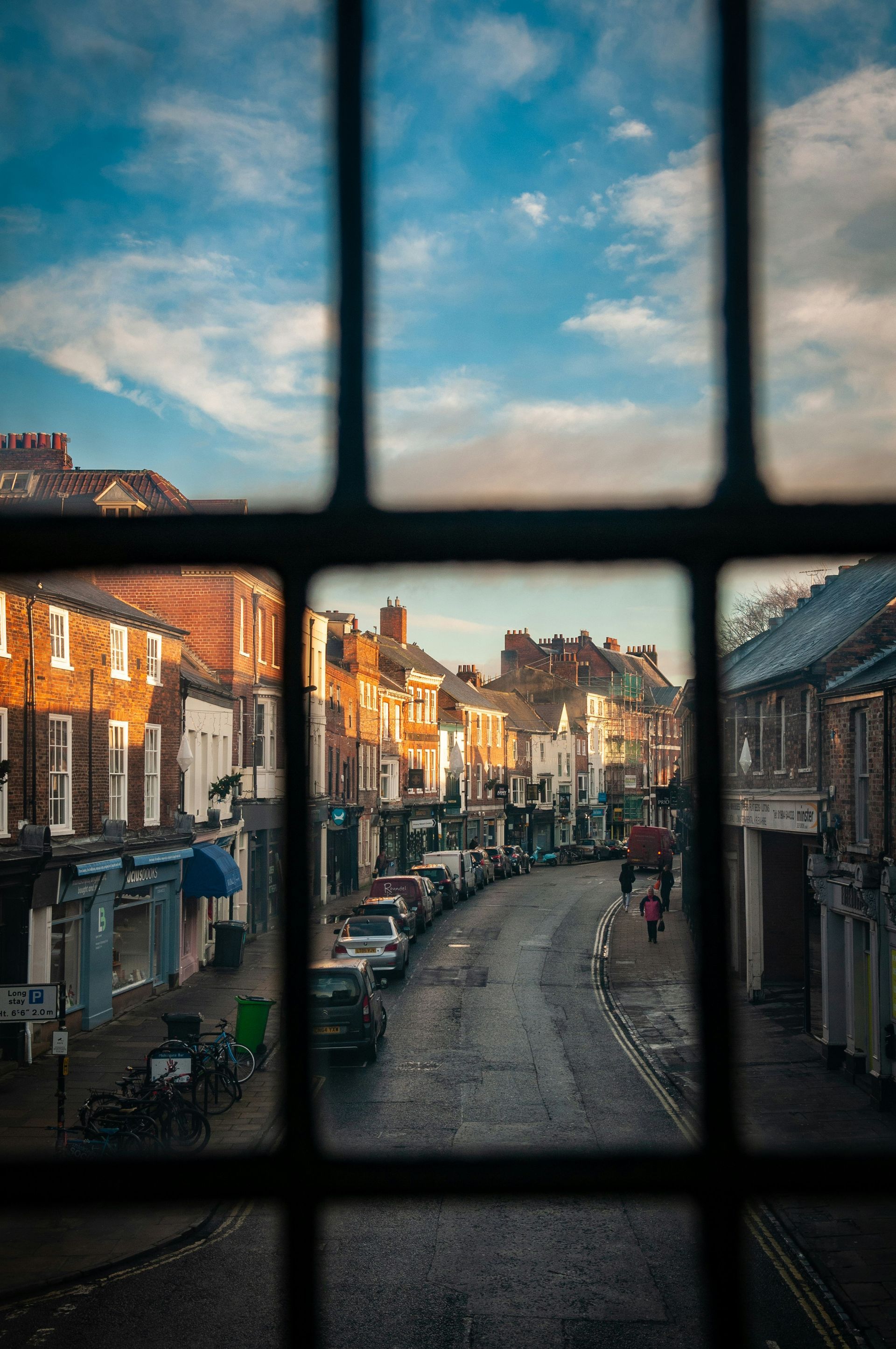 View of a street through a window. Buildings line the road, and cars are parked on the sides in York, England.