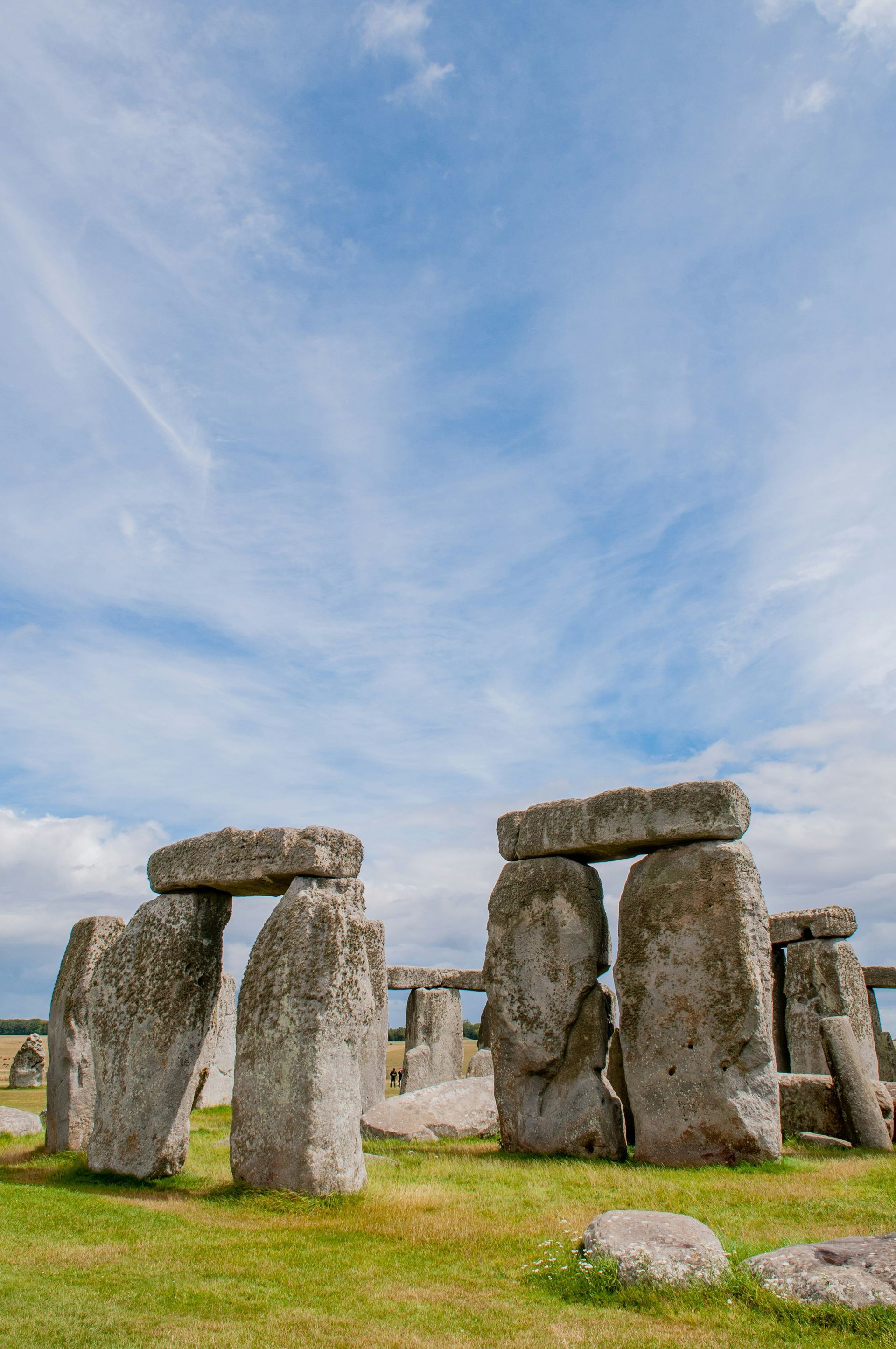 Stonehenge monument on a grassy field under a partly cloudy blue sky in England.