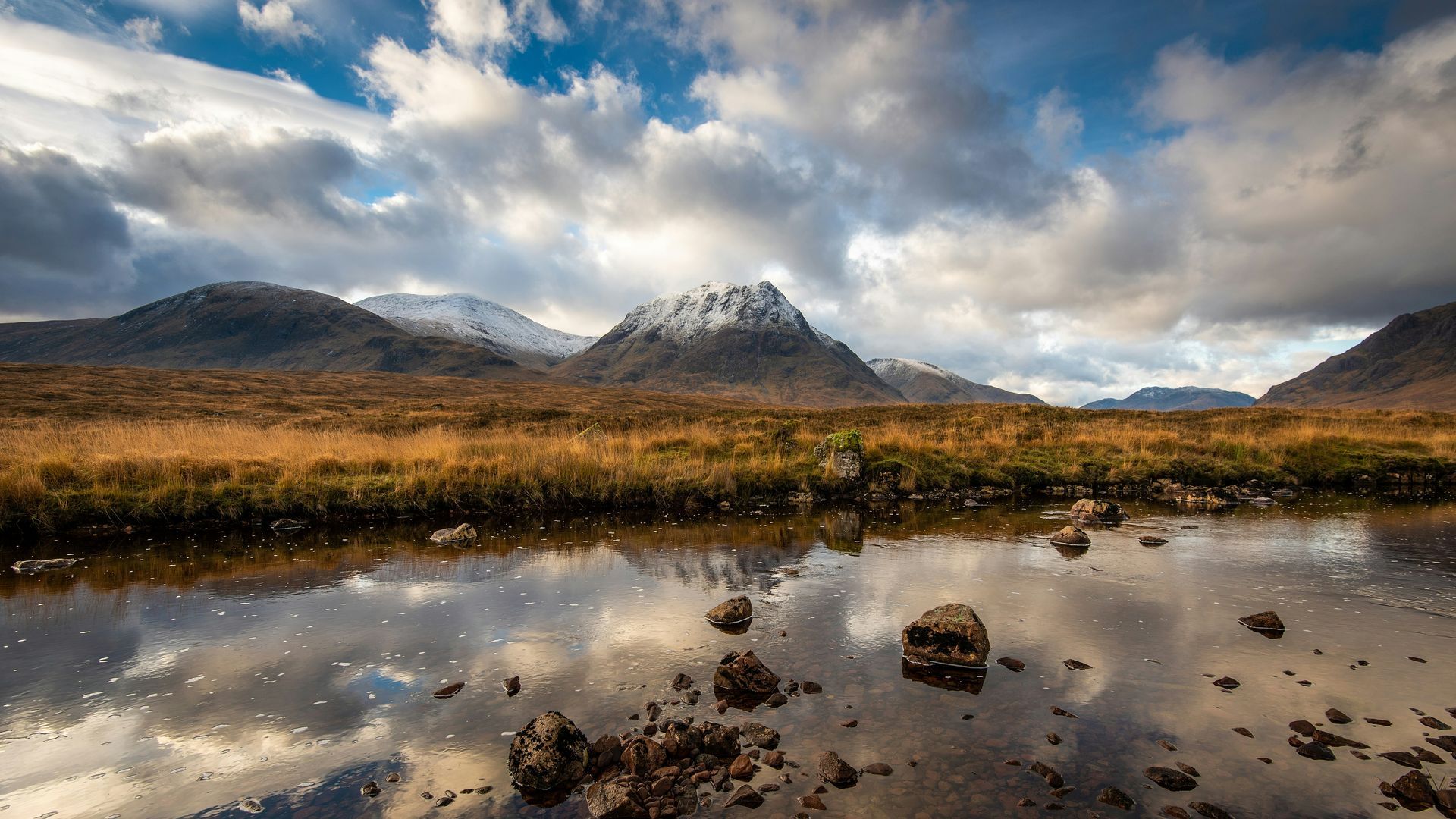 Mountains reflected in water with cloudy sky in Glencoe, Scotland.