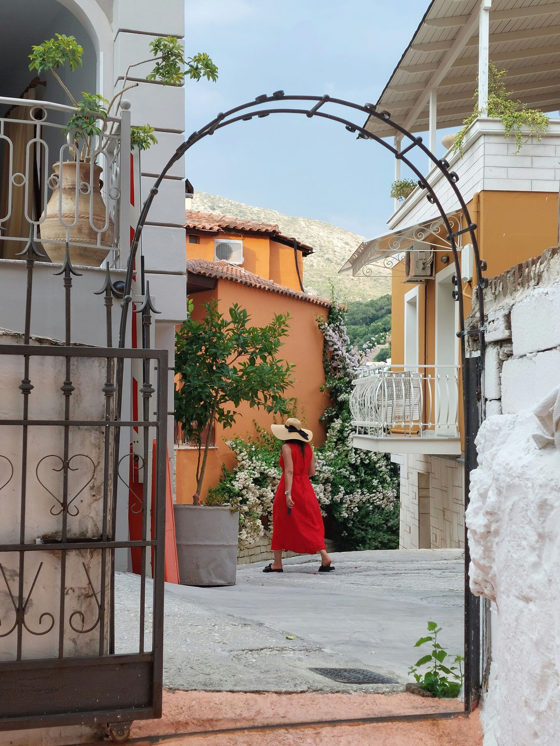 A woman in a red dress is walking through a gate in Parga, Greece.