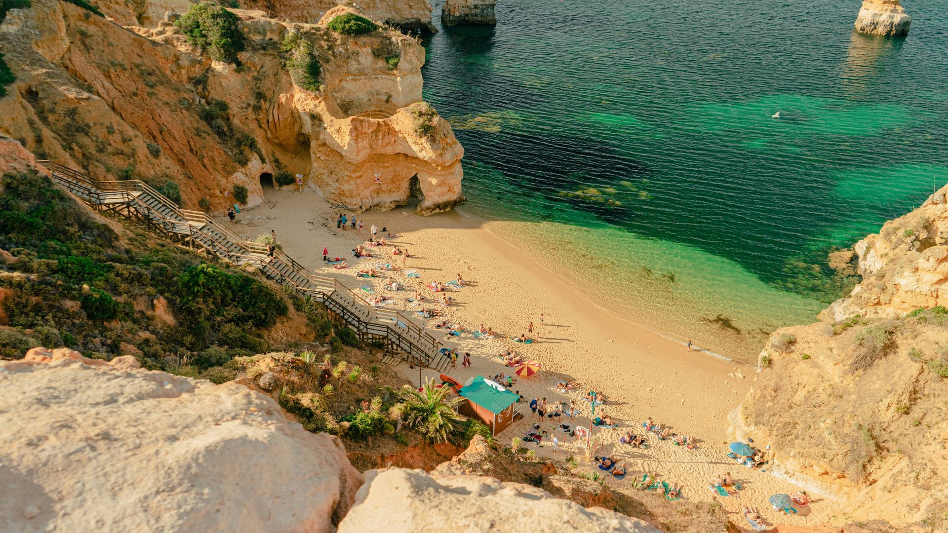Beach with golden sand, turquoise water, cliffs, and sunbathers in Lagos, Portugal.