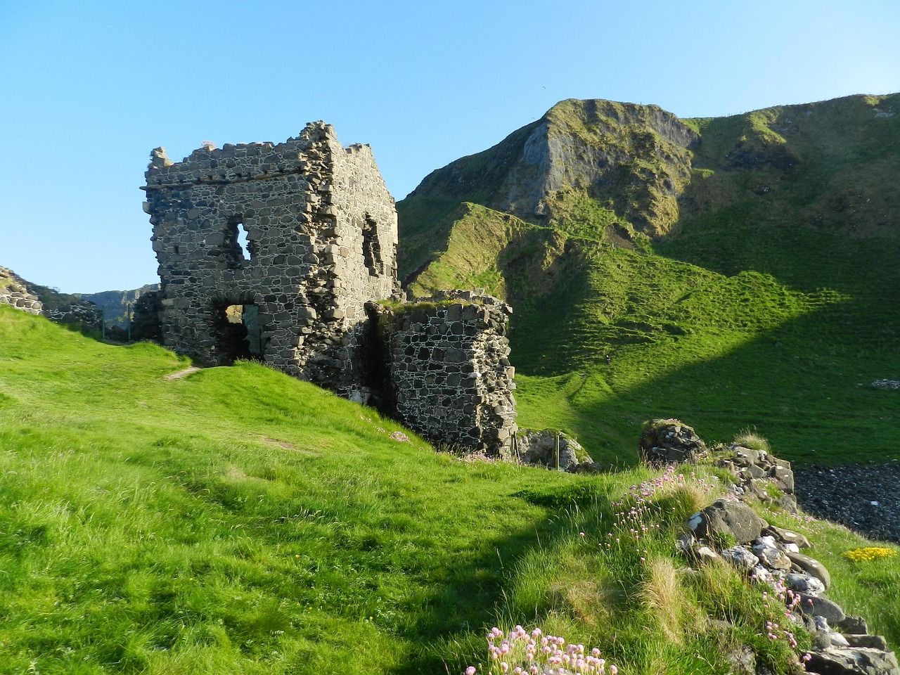 Ruins of a stone castle on a grassy hill with a mountain in the background under a clear sky on the Aran Islands, Ireland.