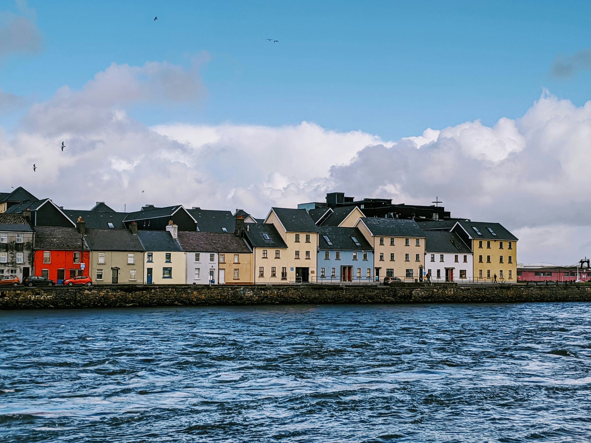 Row of colorful houses along a waterfront in Galway, Ireland. Bright blue sky, and water with some waves.
