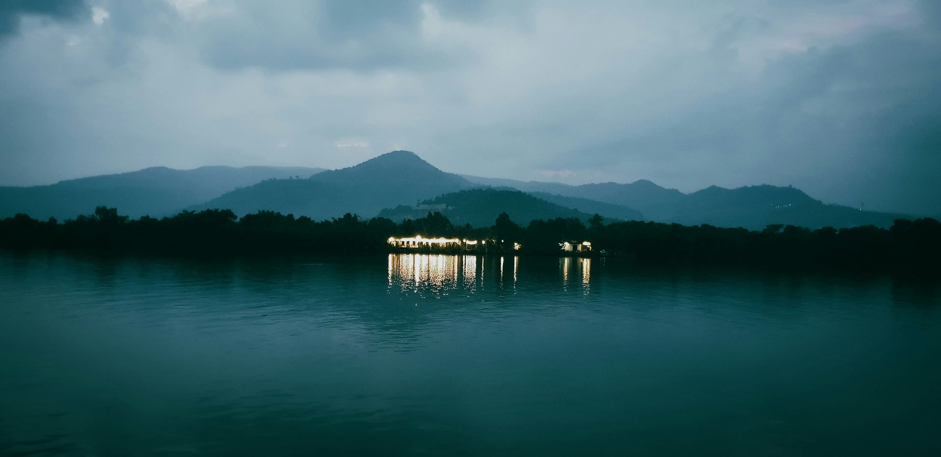 A dark lake with mountains and a building, reflecting lights in Kampot, Cambodia.
