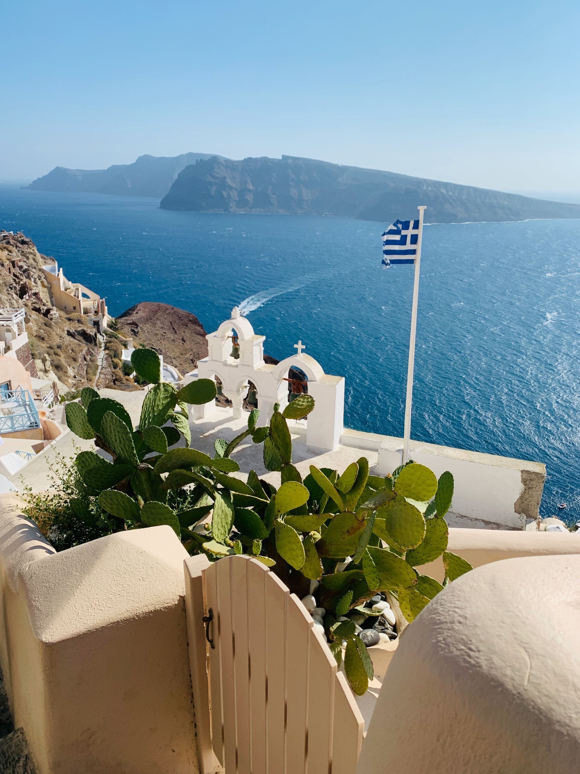 A greek flag is flying over a body of water in Santorini, Greece.