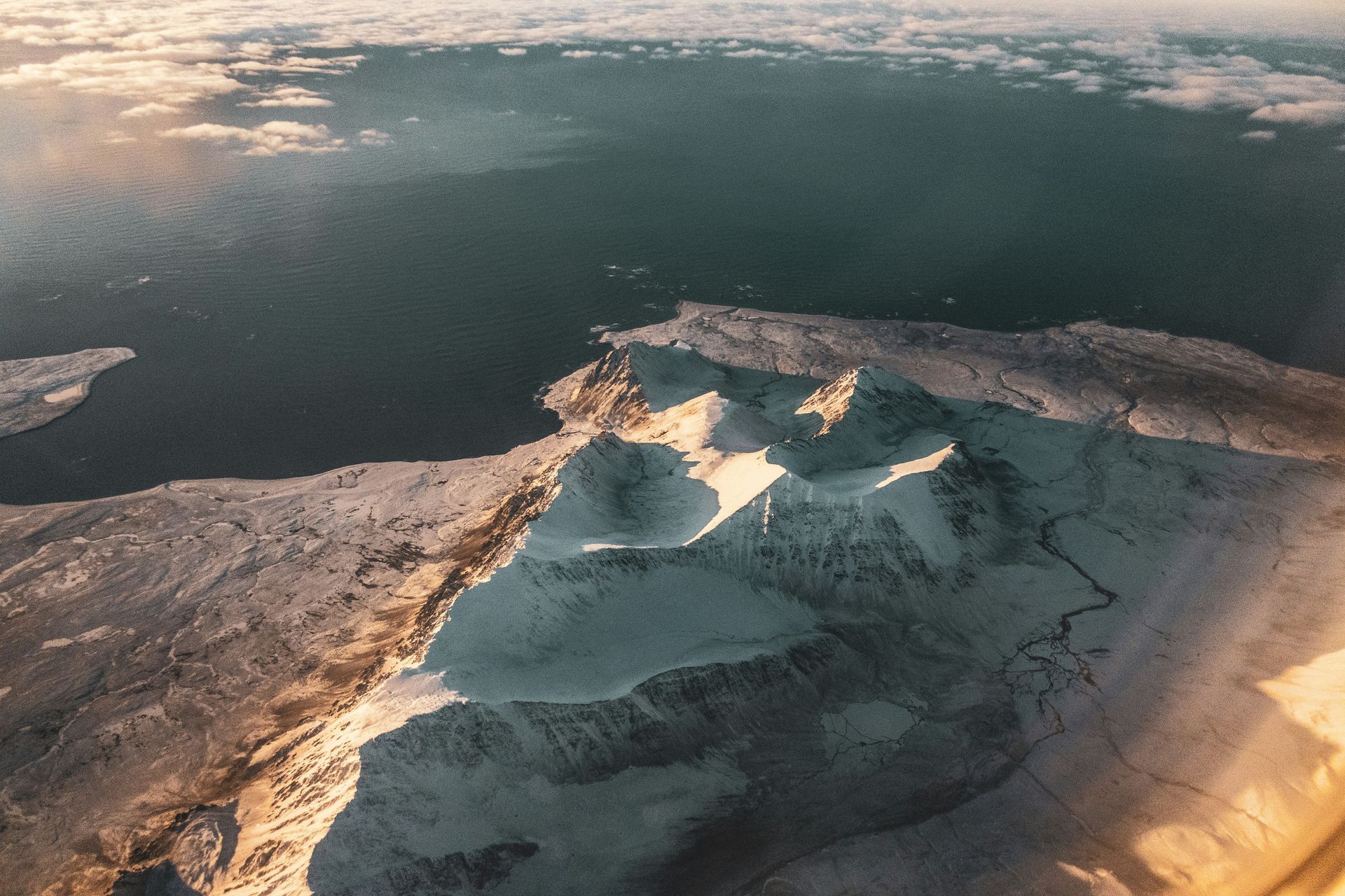 Snow-covered mountains meet the sea. Sunlight bathes the peaks and icy shoreline in Svalbard, Norway.