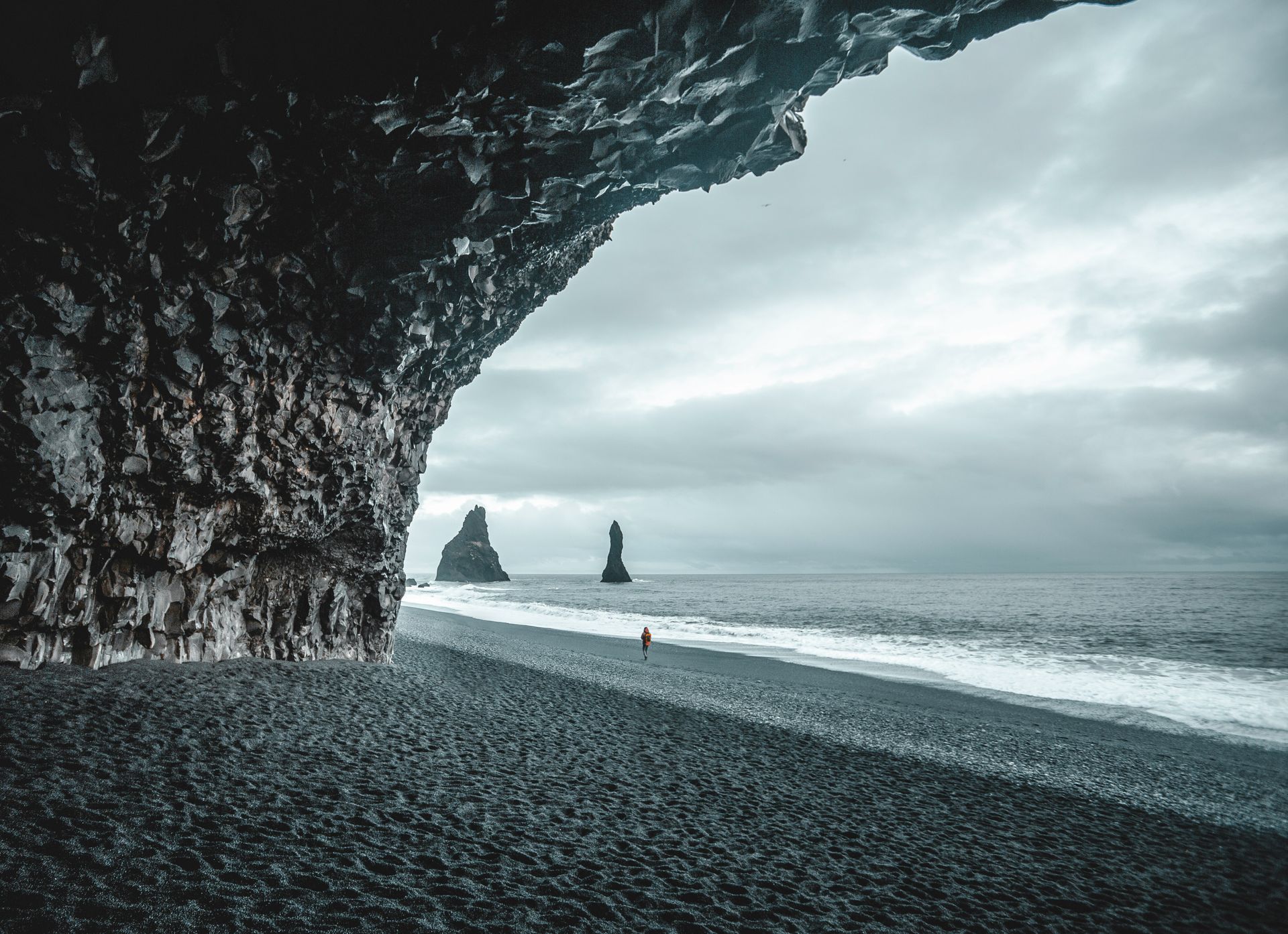 A dark, rocky cave entrance frames a black sand beach with sea stacks in the distance at Reynisfjara Beach Iceland.