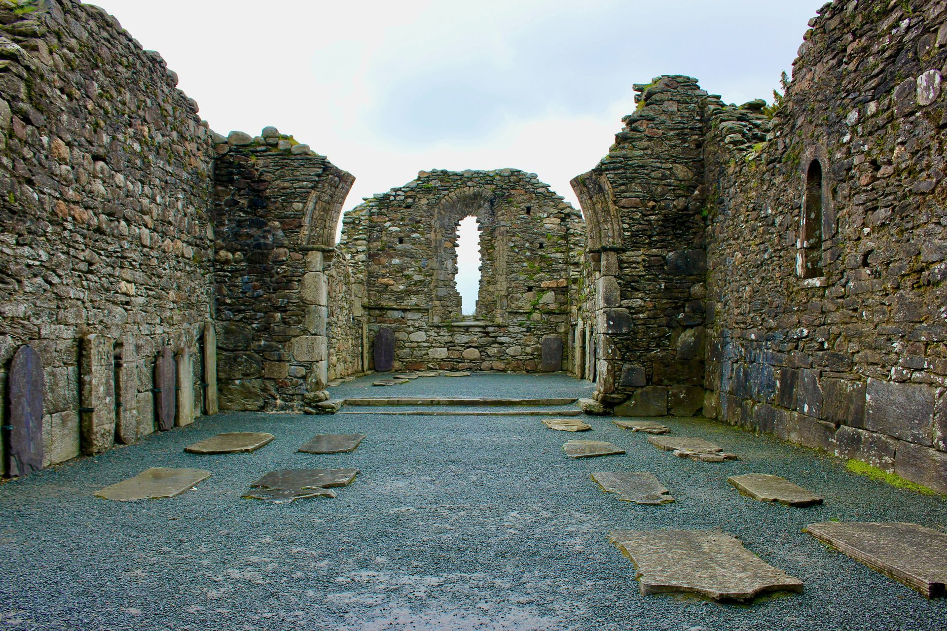 Ruined stone church interior, headstones on the floor, arched windows in Glendalough, Ireland.