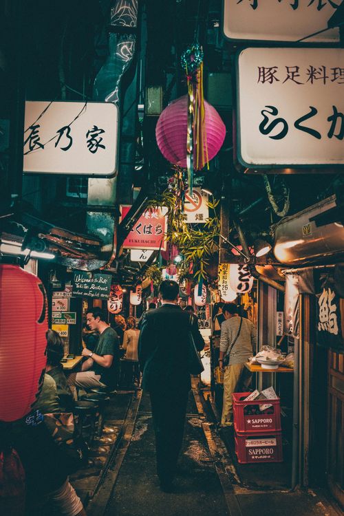 A man is walking down a narrow alleyway with chinese writing on the signs.