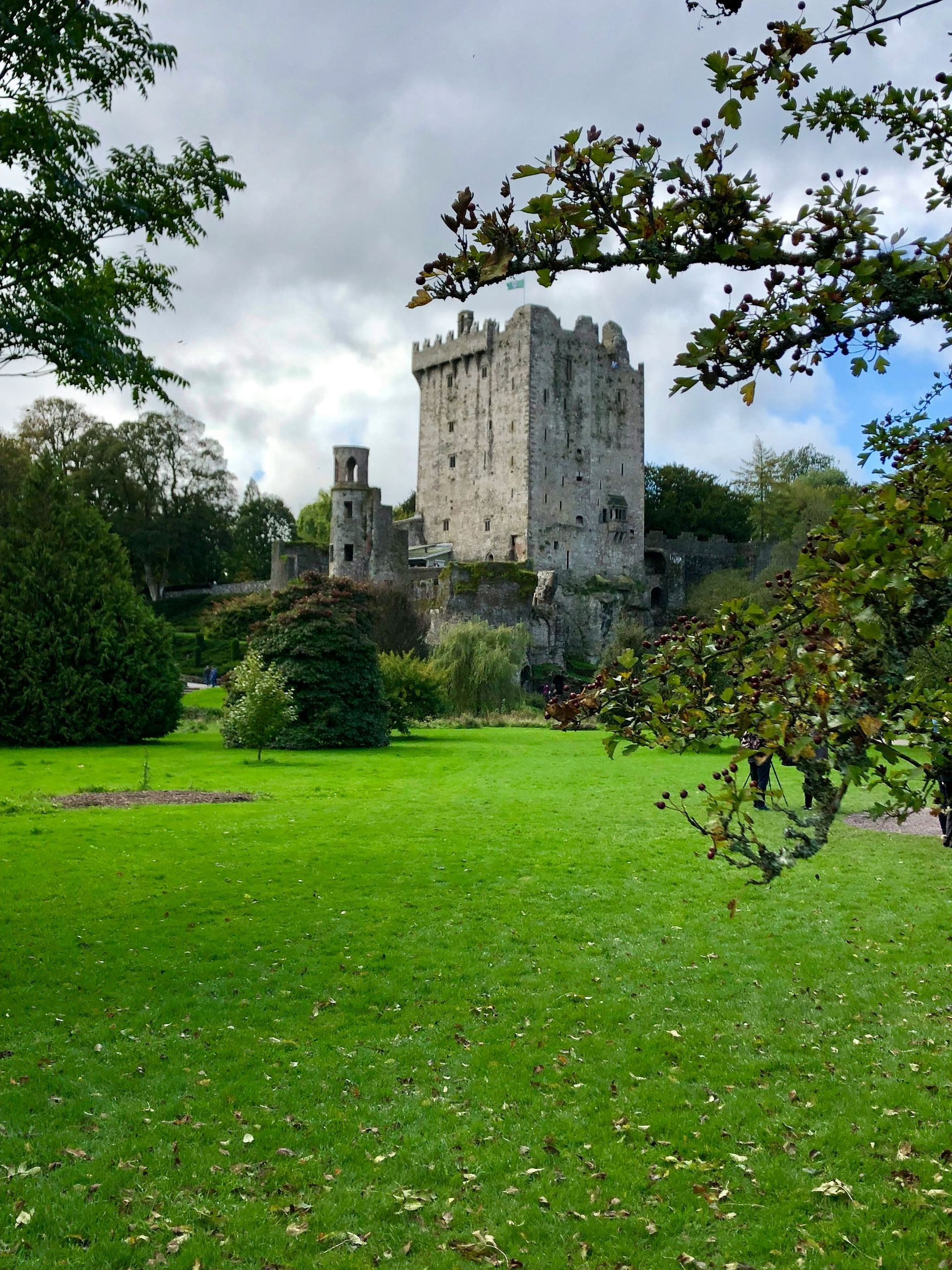 The Blarney Castle with a tower and green lawn under a cloudy sky in Cork, Ireland.