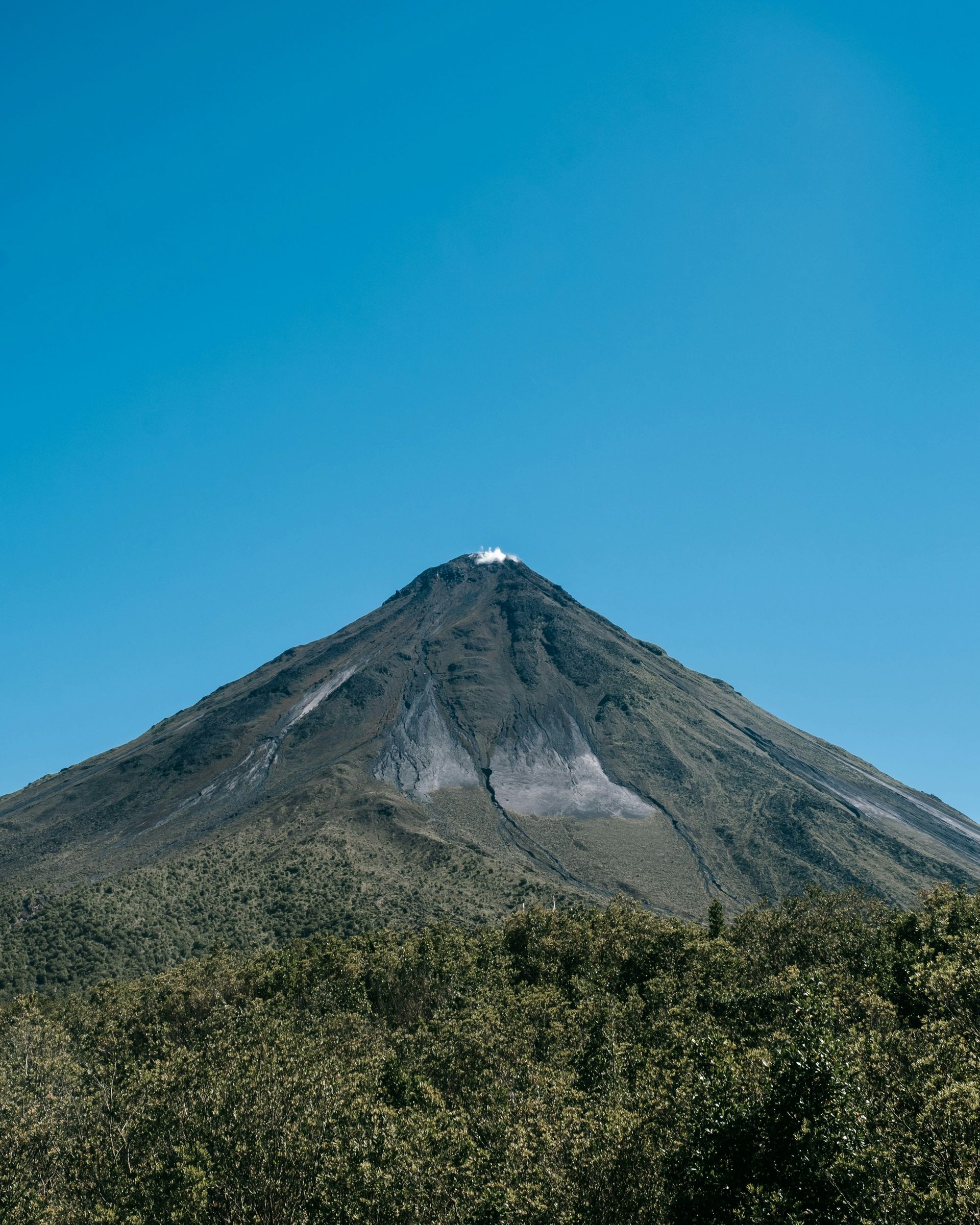 The Arenal Volcano mountain against a clear blue sky. Lush green foliage in the foreground in Costa Rica.
