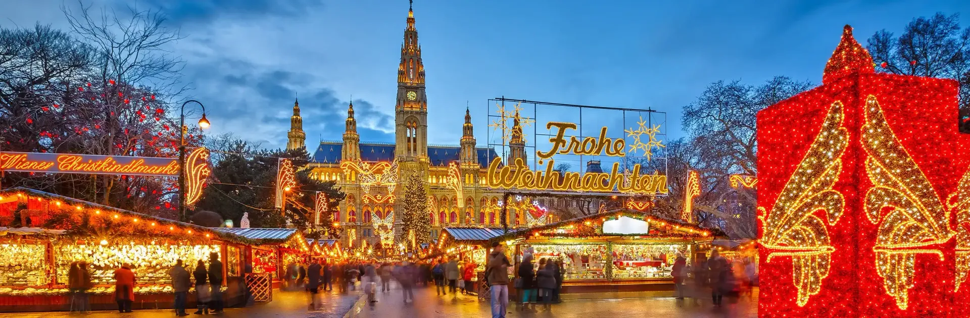 A festive scene at a Christmas market with bright lights and a large building in the background in Germany.